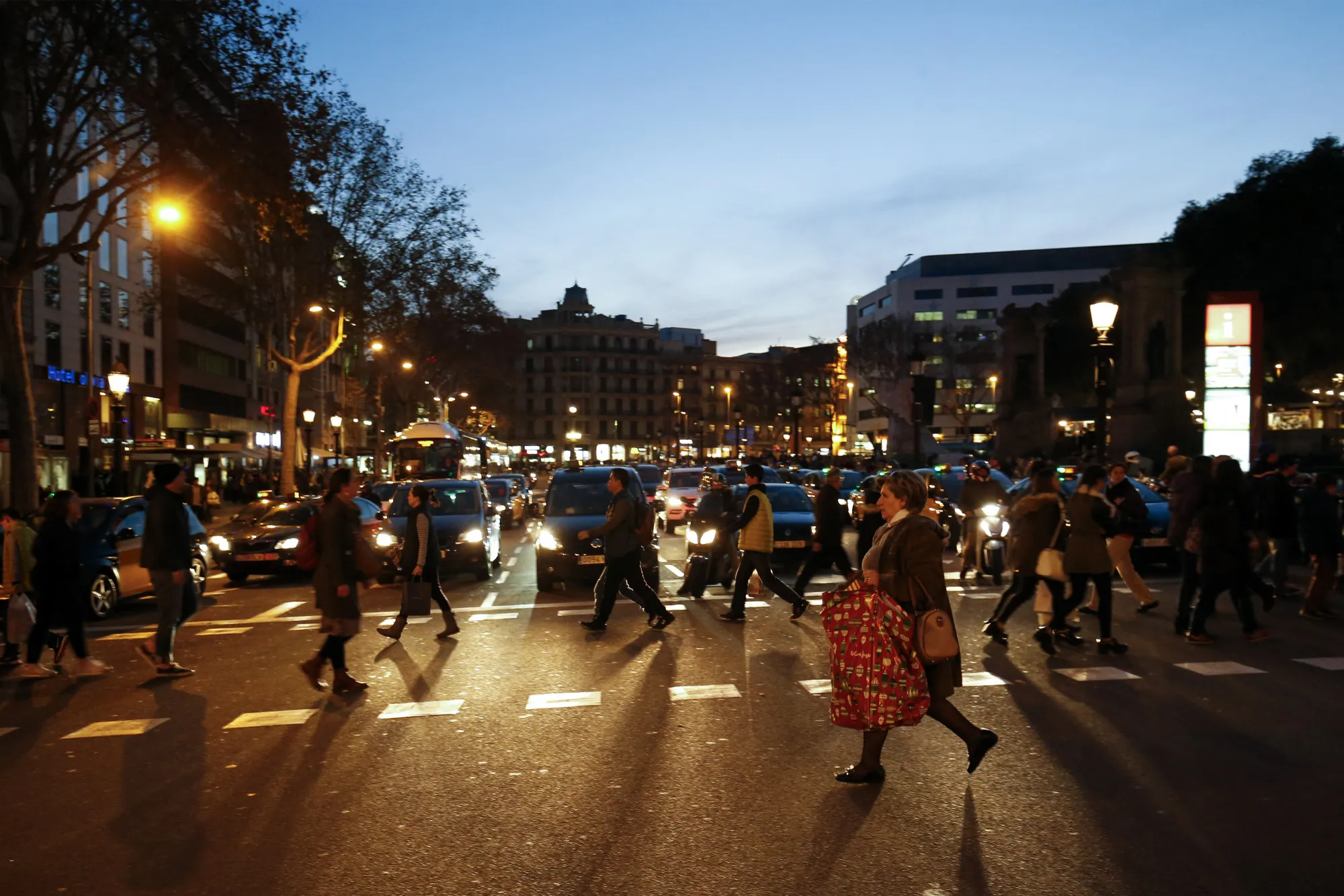 Pedestrians and shoppers cross a road on a shopping street in Barcelona.

