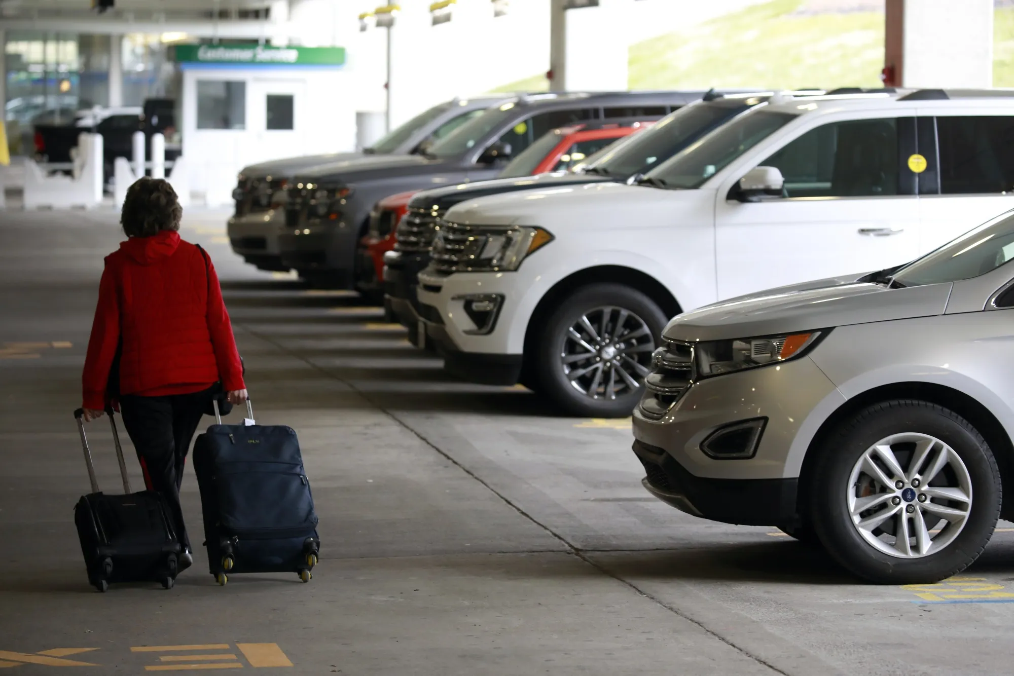 A traveler pulls luggage past rental vehicles at a Hertz location in Louisville, Kentucky