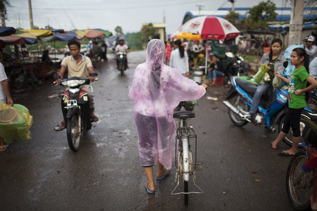 A woman pushes her bicycle past a market in a garment manufacturing district in Phnom Penh, Cambodia.
