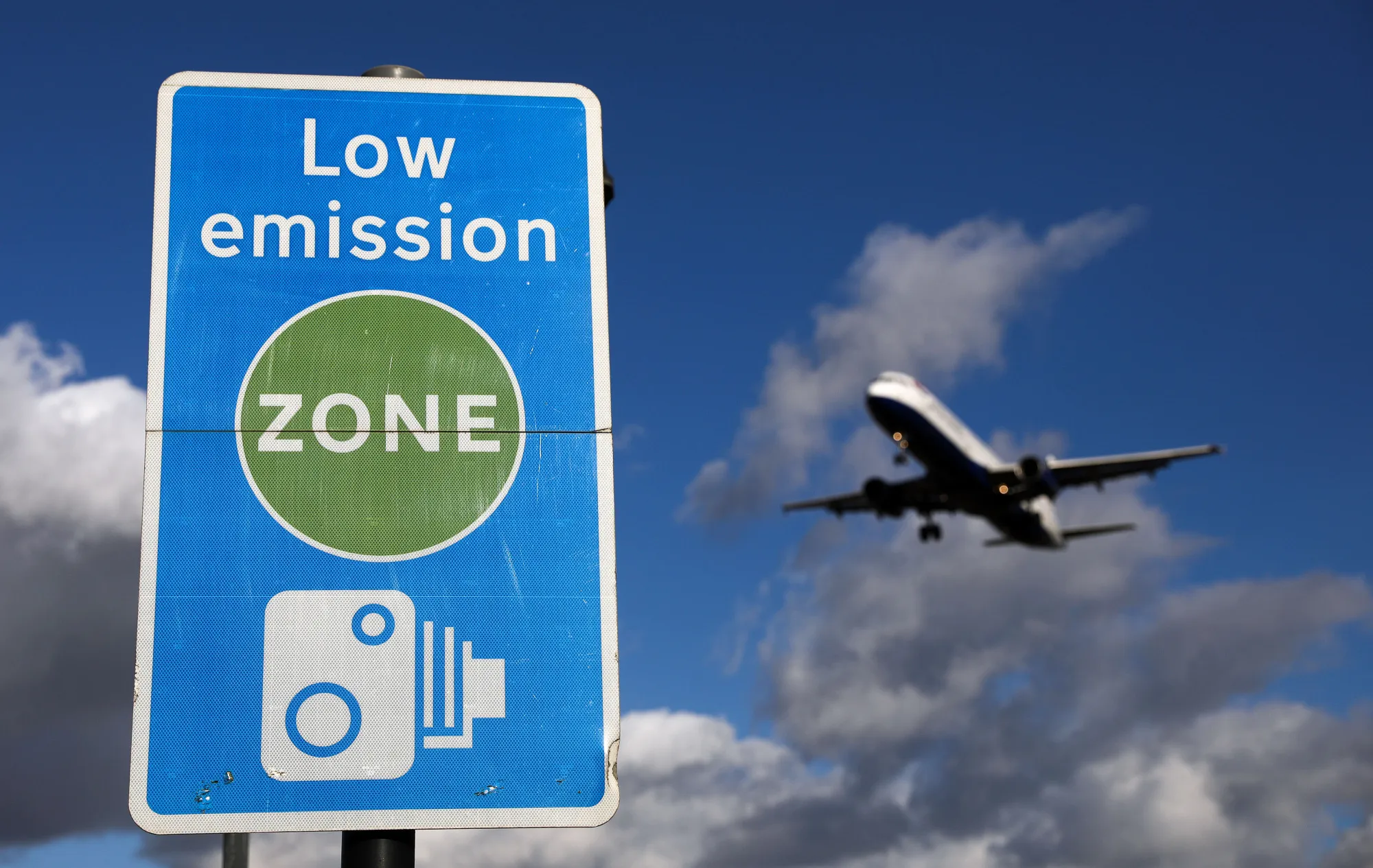 An aircraft passes a low emission zone sign as it prepares to land at Heathrow airport.