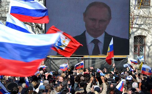 People Wave Russian Flags as President Putin is seen on a Screen