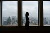 A woman is silhouetted while looking out of a window of an office building.