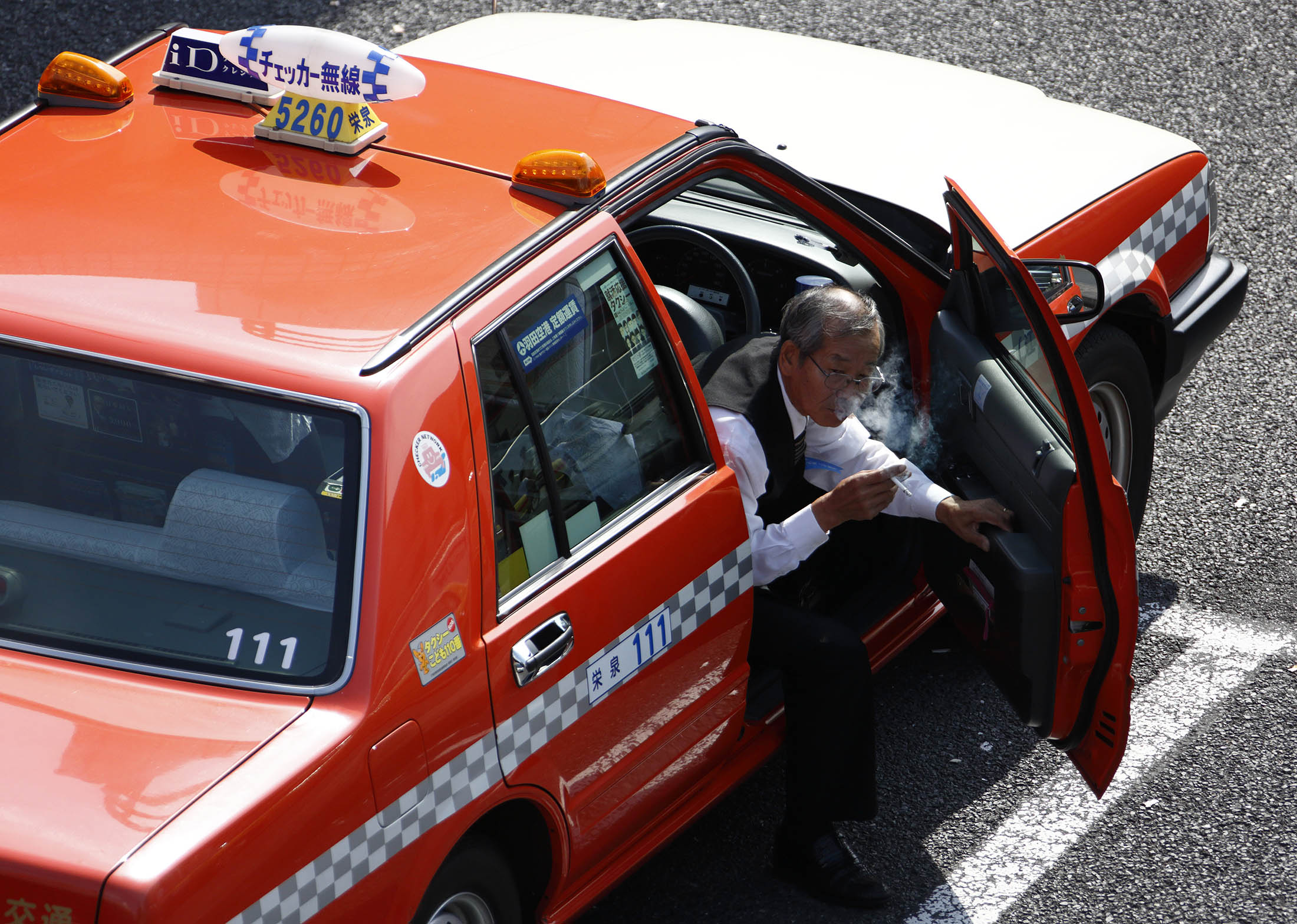 A taxi driver smokes as he exits a taxi outside a train station in Tokyo, Japan, on Wednesday, Sept. 23, 2015. Tokyo's taxi companies will shift as much as 30 percent of their fleets to an LPG-powered hybrid from Toyota Motor Corp. by 2020, raising the bar for the world’s biggest cities in their bids to reduce emissions from cabs.
