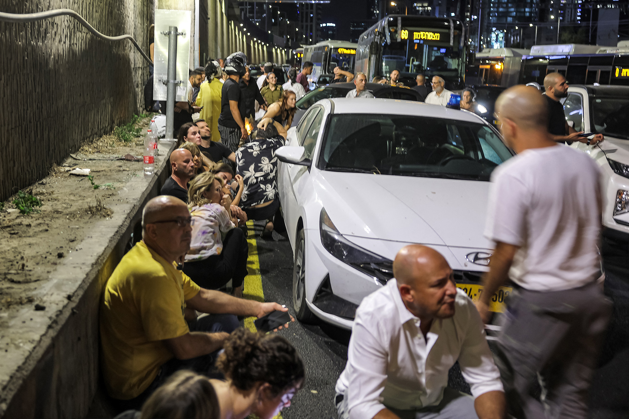 People take cover behind vehicles under a bridge along the side of a highway in Tel Aviv on Oct. 1.