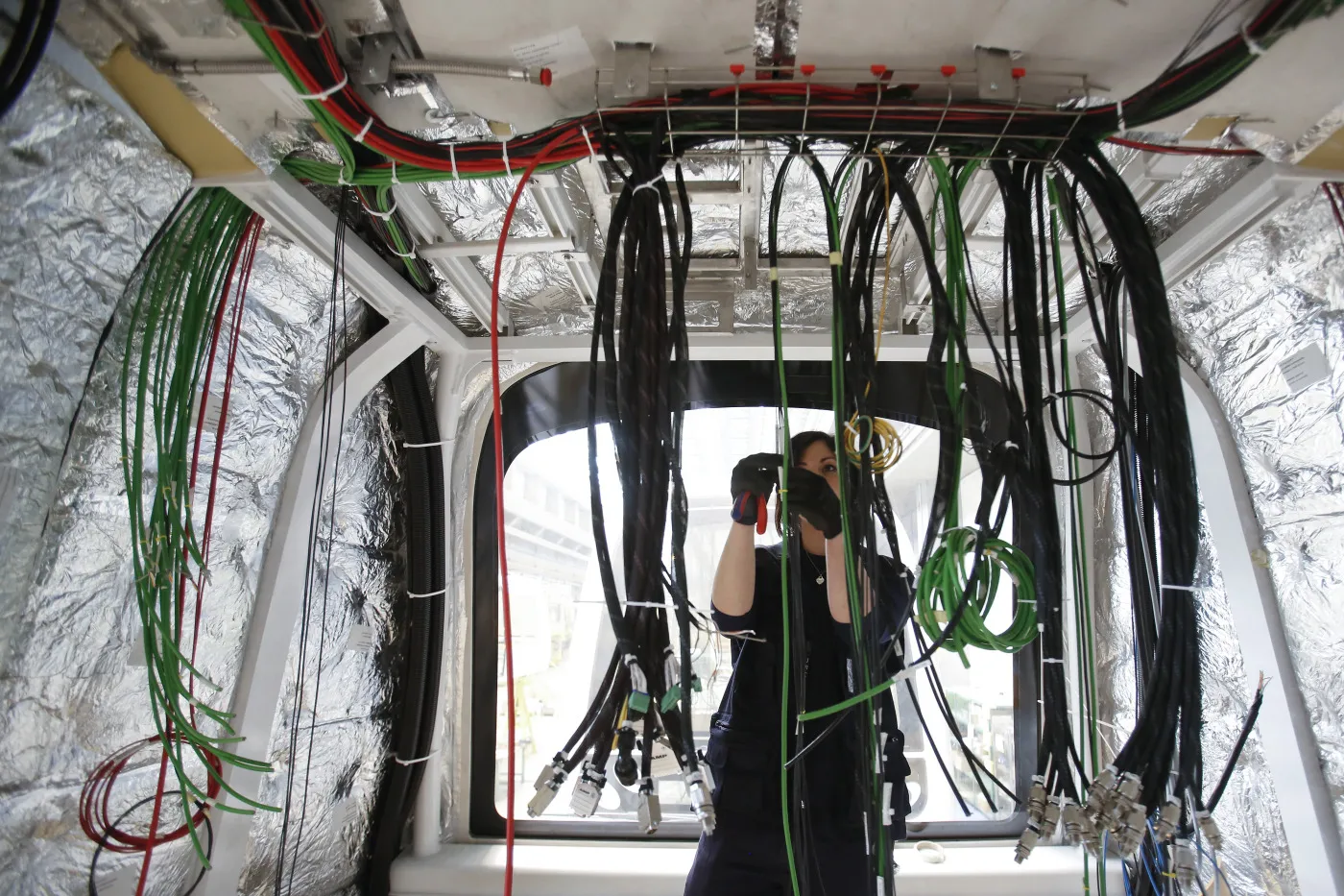 An employee works on electric cabling inside the shell of a metro train carriage during manufacture at rail car plant in Naples, Italy.