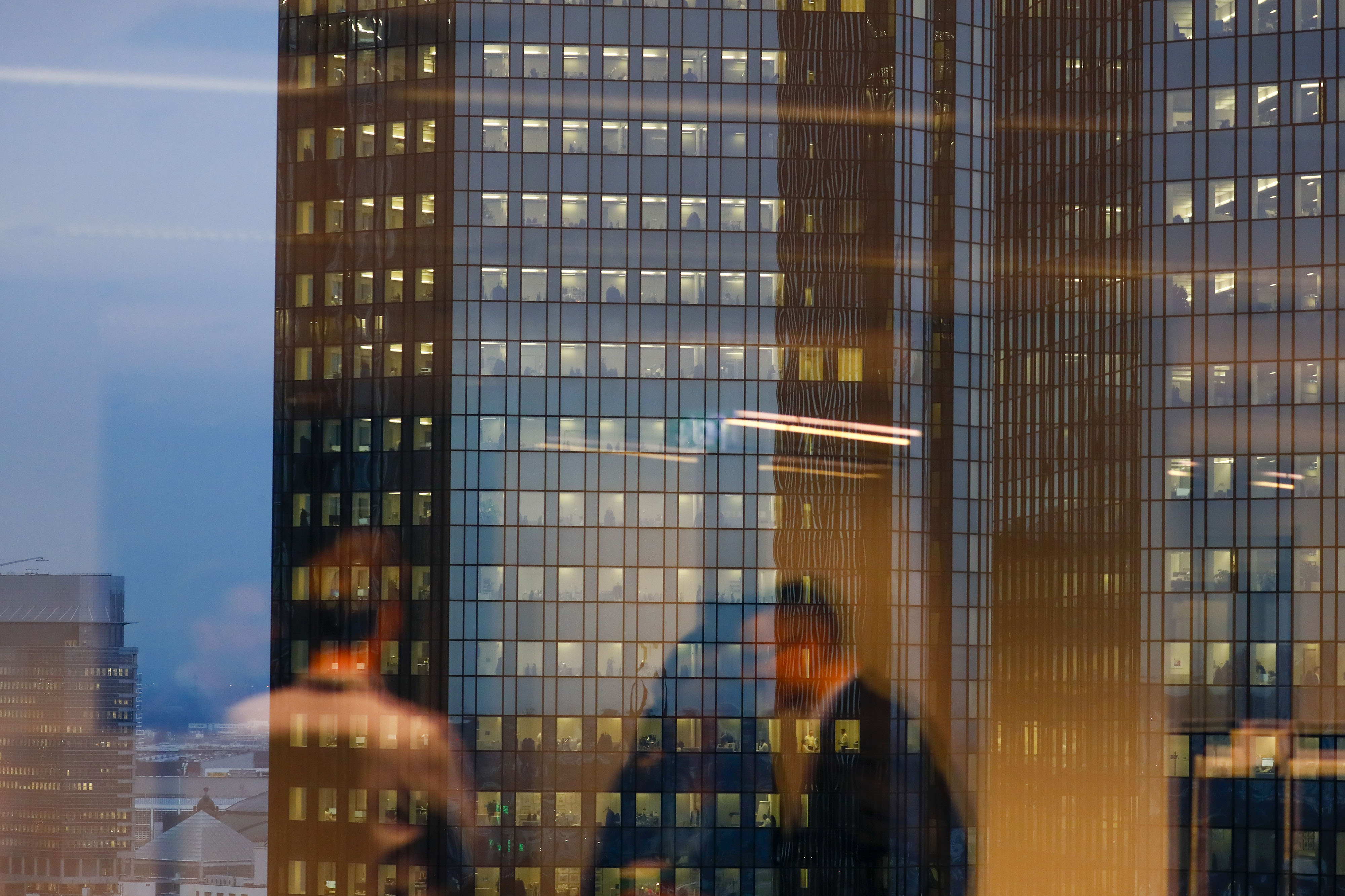 City workers are reflected in an office window opposite the Deutsche Bank AG headquarters in&nbsp;Frankfurt.