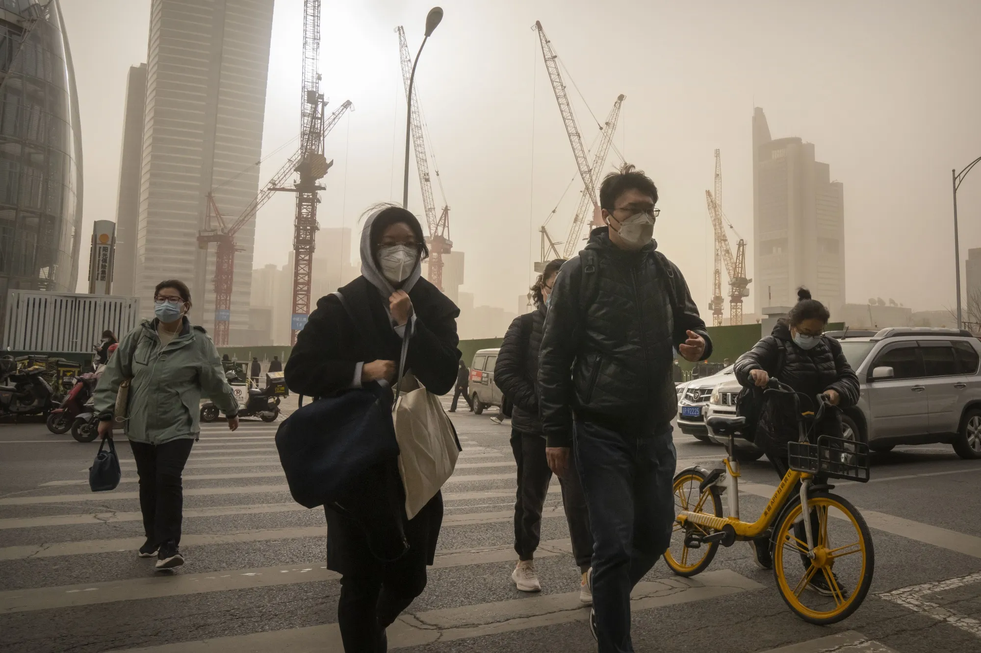 People wearing face masks walk across a street in the central business district in Beijing on March 22.