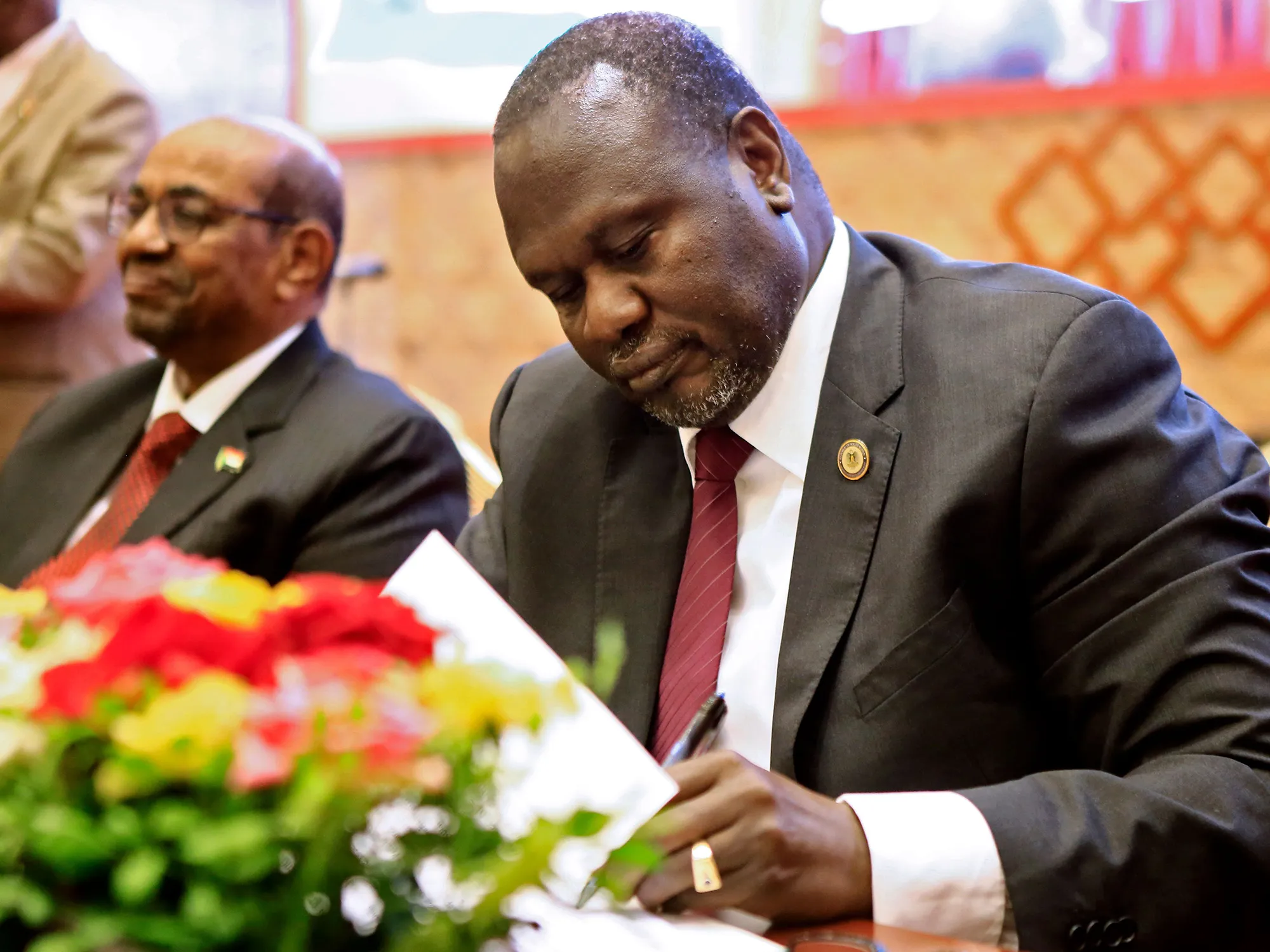 South Sudanese rebel leader Riek Machar, right,&nbsp;signs documents as Sudanese President Omar al-Bashir, left,&nbsp;is seated&nbsp;in Khartoum on June 27, 2018.
