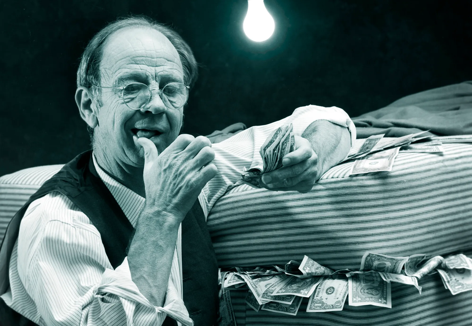 An elderly gentleman licks his thumb while counting money stashed underneath his mattress, 1972.&nbsp;