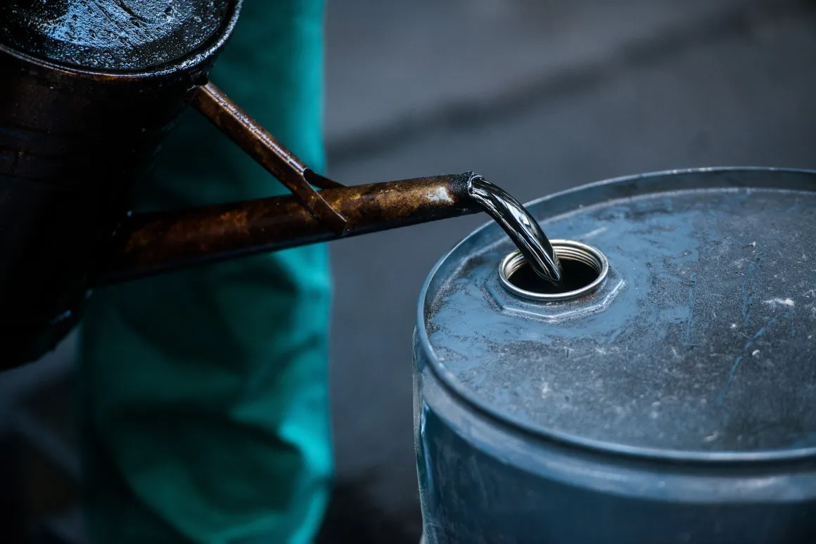 A worker pours liquid oil into a barrel at an&nbsp;oil refinery.