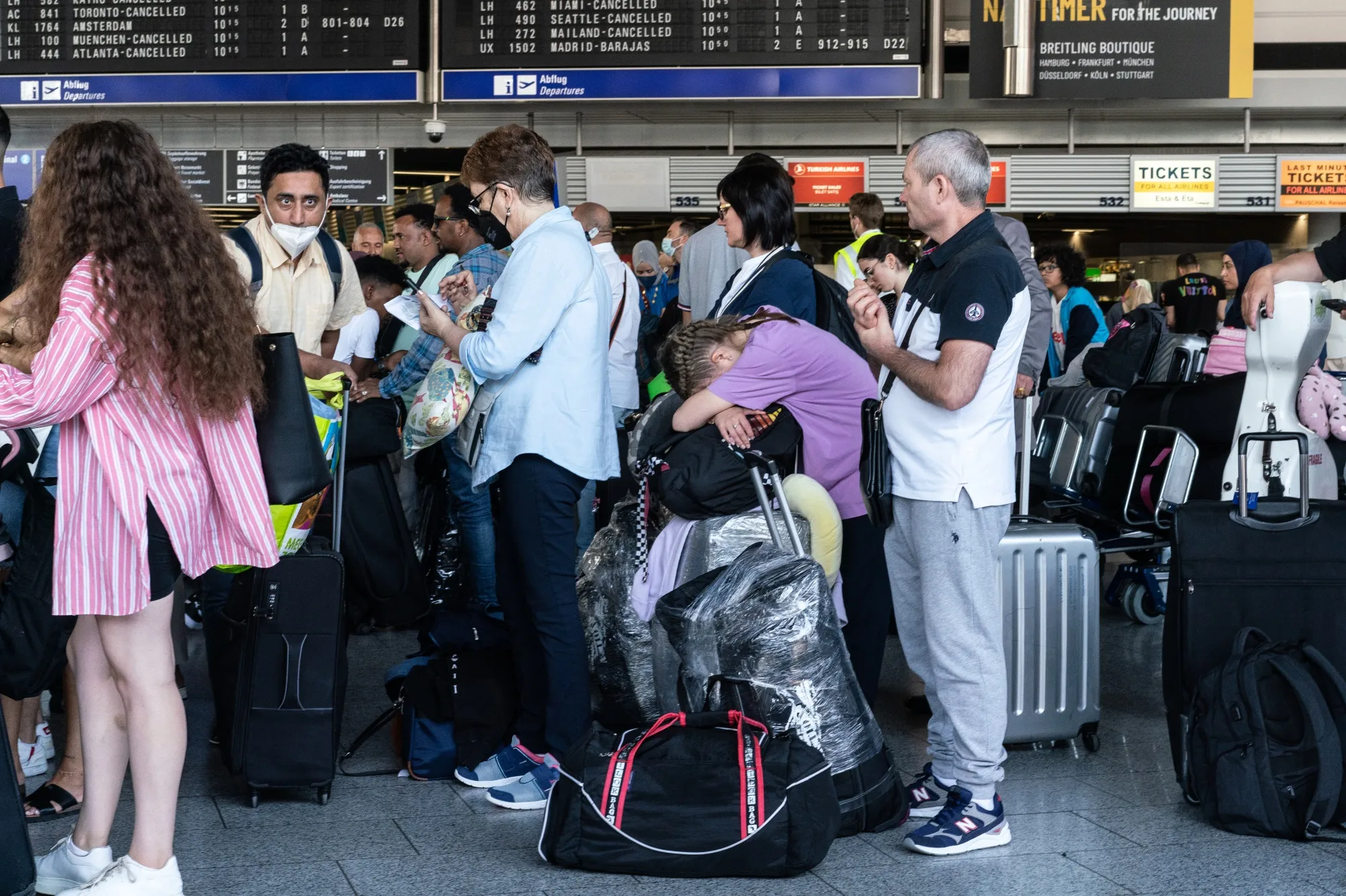 Travelers queue in front of flight information boards displaying canceled flights at Frankfurt Airport in July.