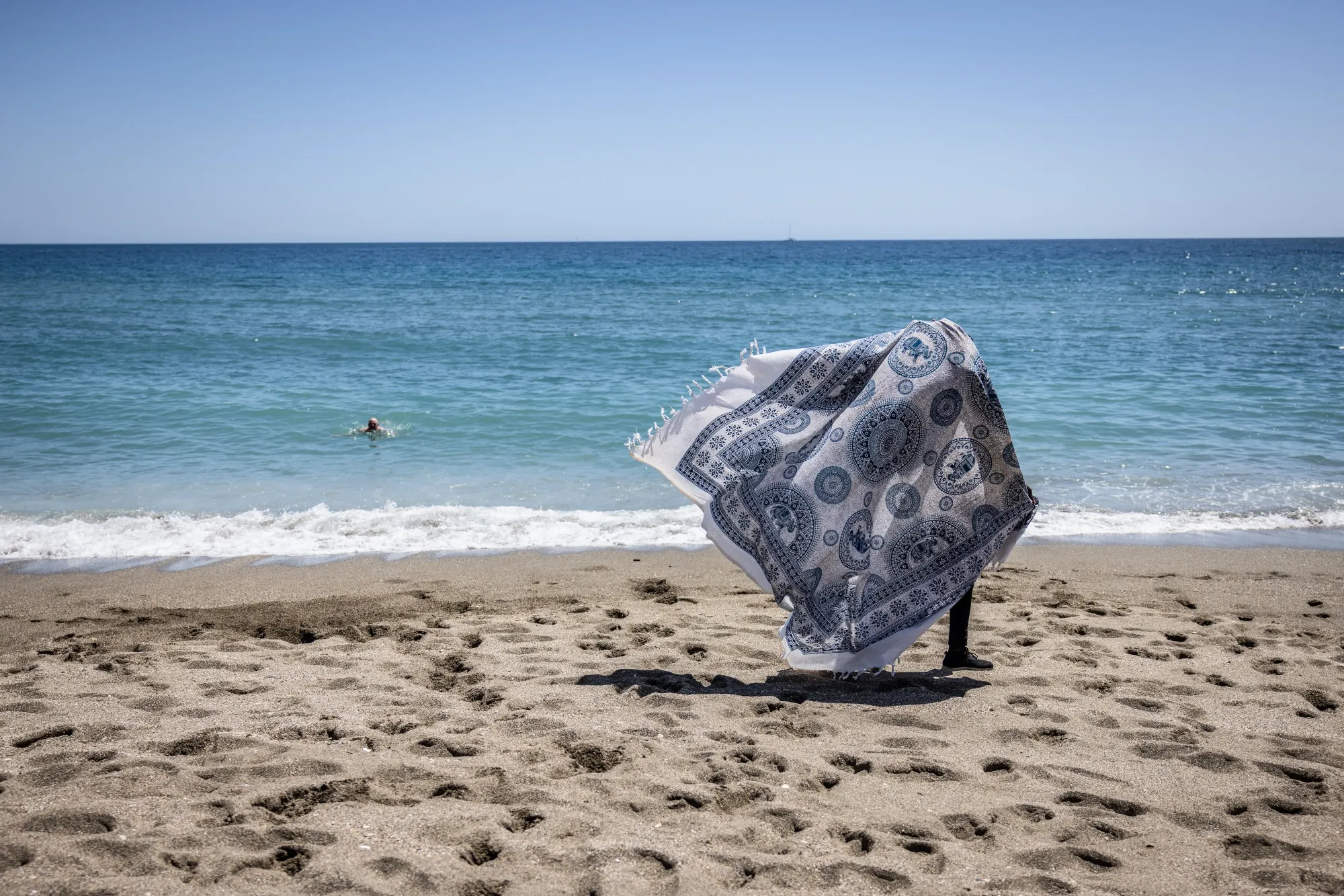 A vendor carries fabric for sale on Malagueta beach in Malaga, Spain.