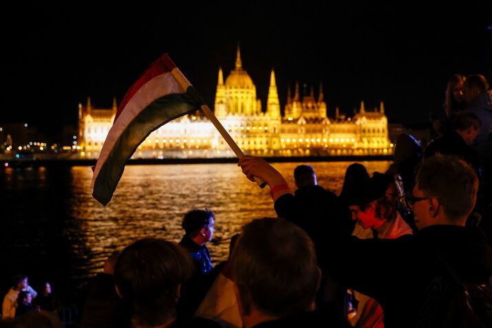 An attendee holds a Hungarian flag during a Tisza party election event across from the Hungarian Parliament.