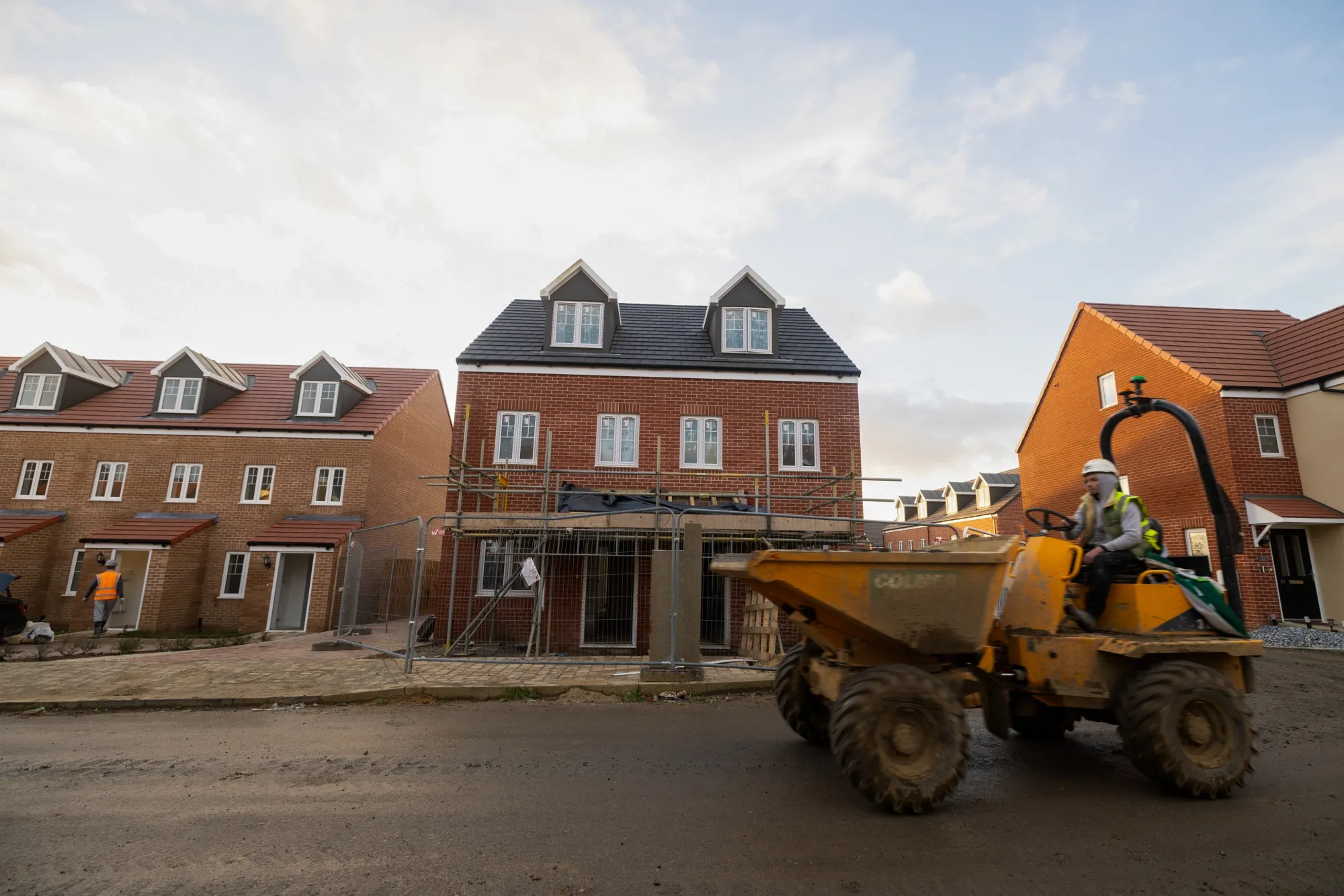 A digger passes a partly completed home on a Persimmon Plc residential property construction site in Harlow, UK.