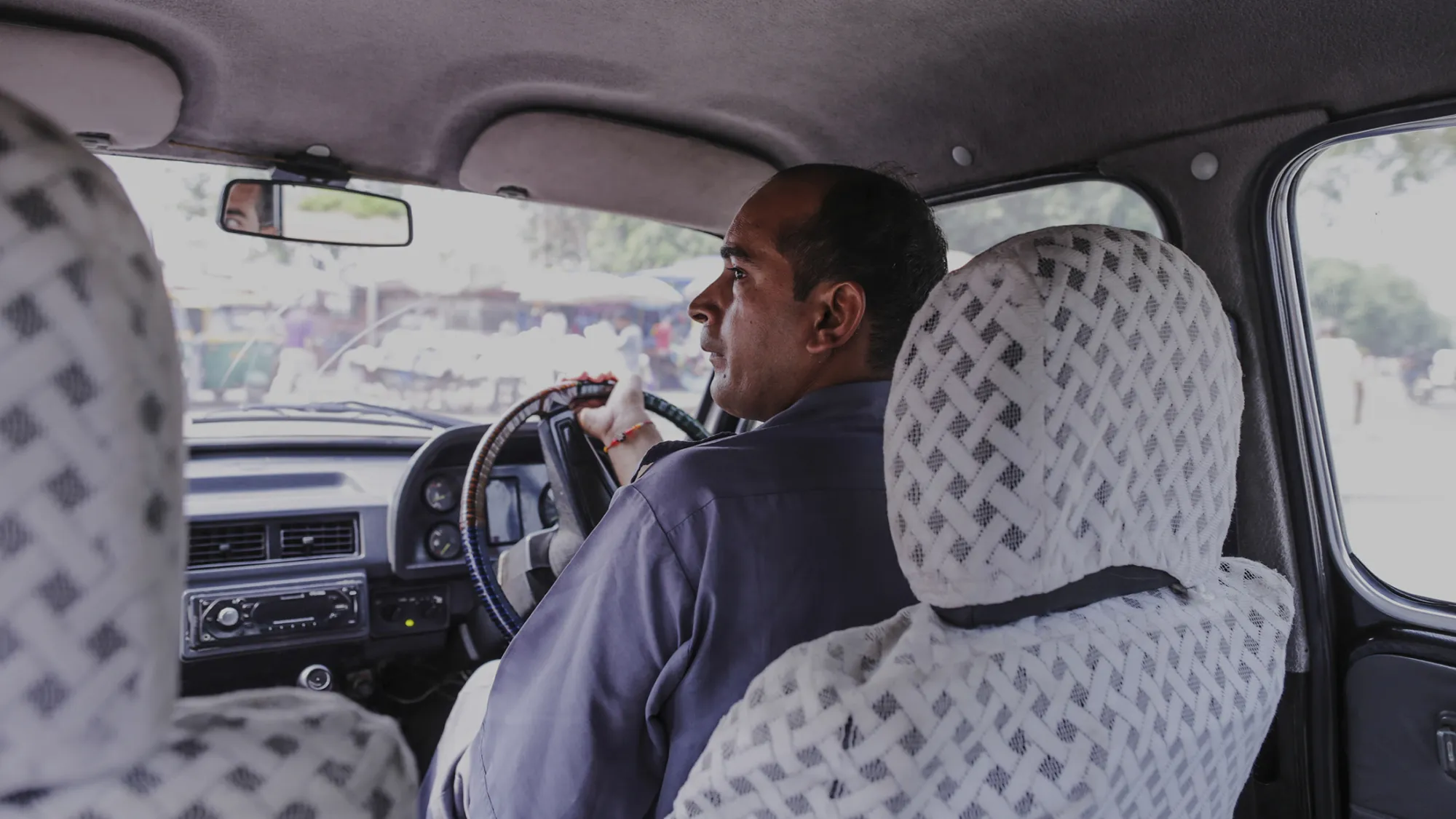 Taxi driver Gurmeet Singh sits inside a Hindustan Motors Ltd. Ambassador taxi as he waits at a traffic light in New Delhi, India, on Saturday, Sept. 19, 2015. As cabs lured by app-based platforms proliferate in India, where car ownership is low and public transportation services in most cities and towns haven’t kept pace with the needs of a growing population, drivers are facing stiffer competition for rides.
