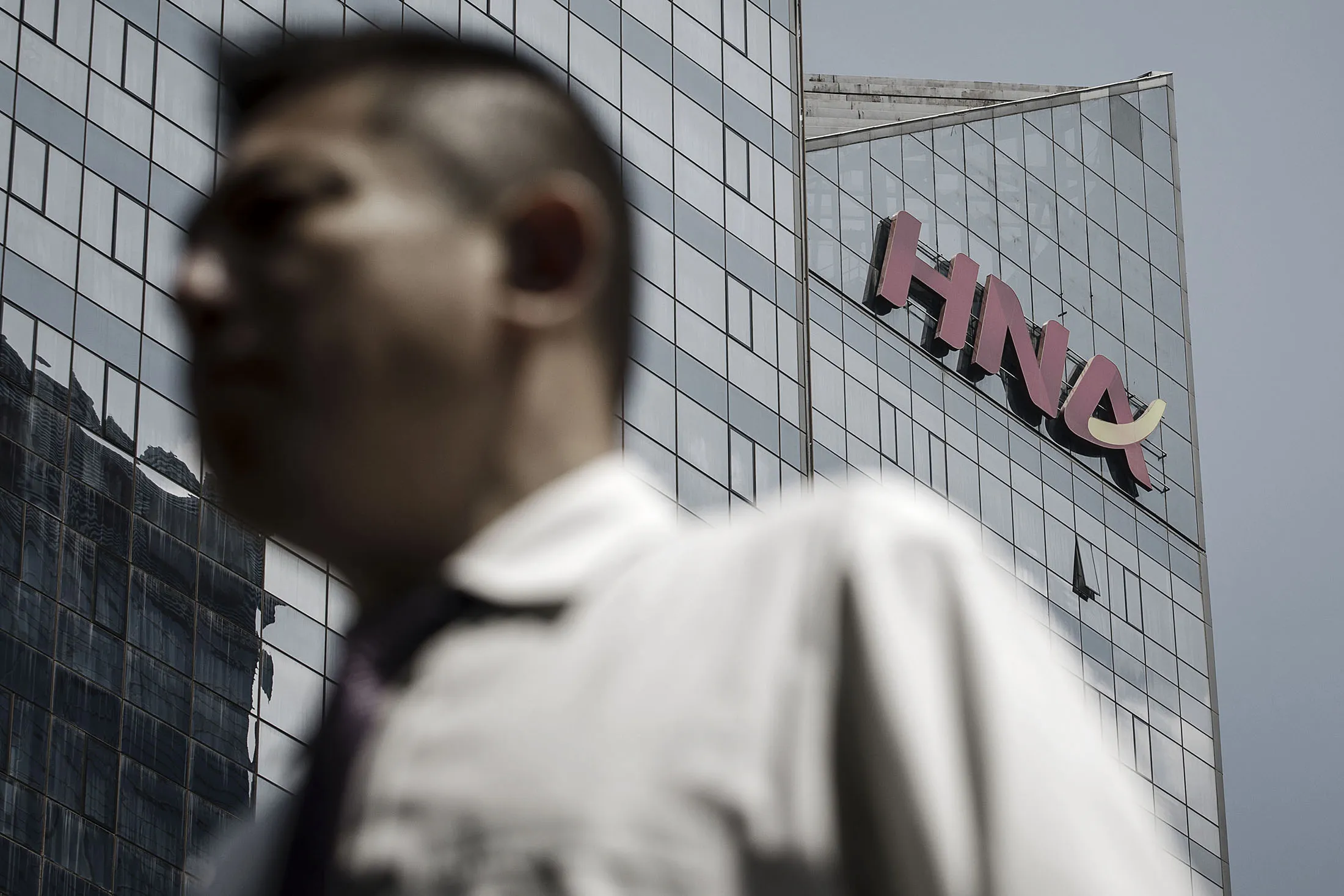 A pedestrian walks past the HNA Group Co. building in Beijing, China, on Wednesday, Aug. 9, 2017. Big Chinese dealmakers including HNA have been under increasing scrutiny this year as the Communist Party steps up its clampdown of capital outflows to protect the yuan from weakening further.