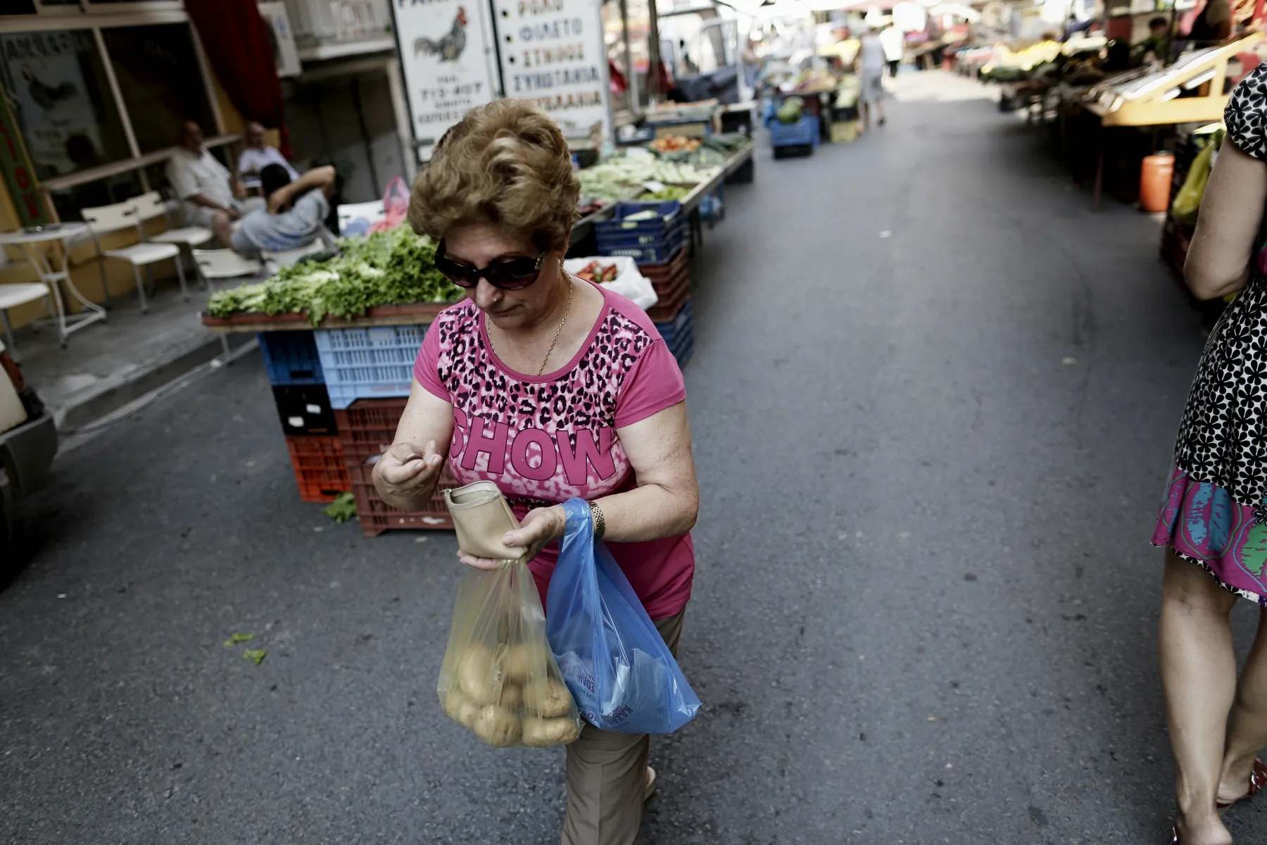 A customer puts coins into her purse while shopping for groceries at a farmer's market in the old town of Thessaloniki.&nbsp;