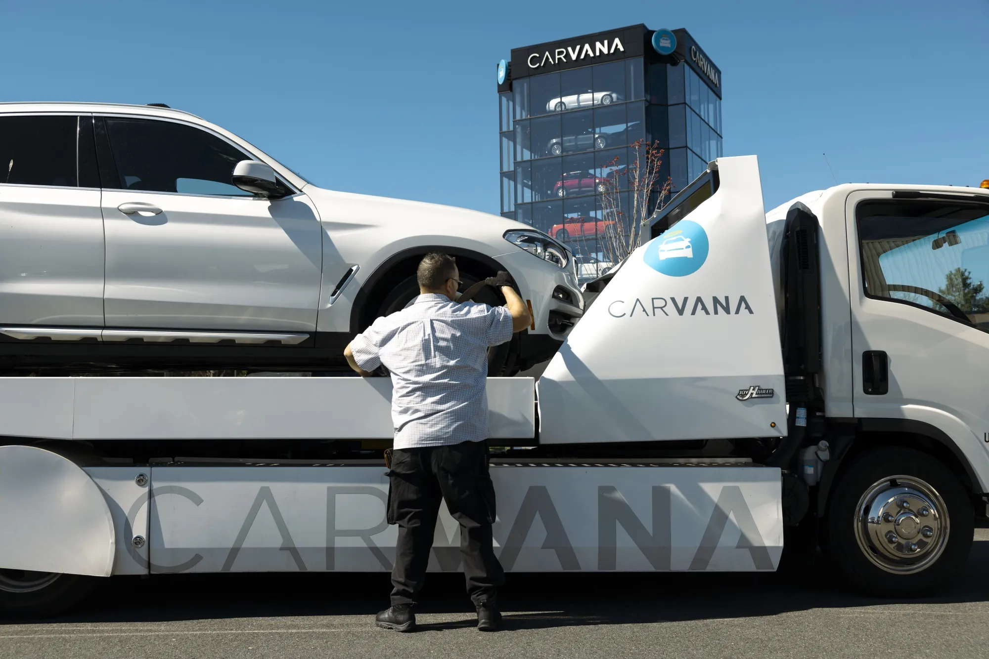 A worker unloads a vehicle from a flatbed truck at a Carvana vending machine location in Uniondale, New York.