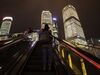 Pedestrians ride escalators as commercial buildings stand illuminated at night in the Lujiazui Financial District in Shanghai.