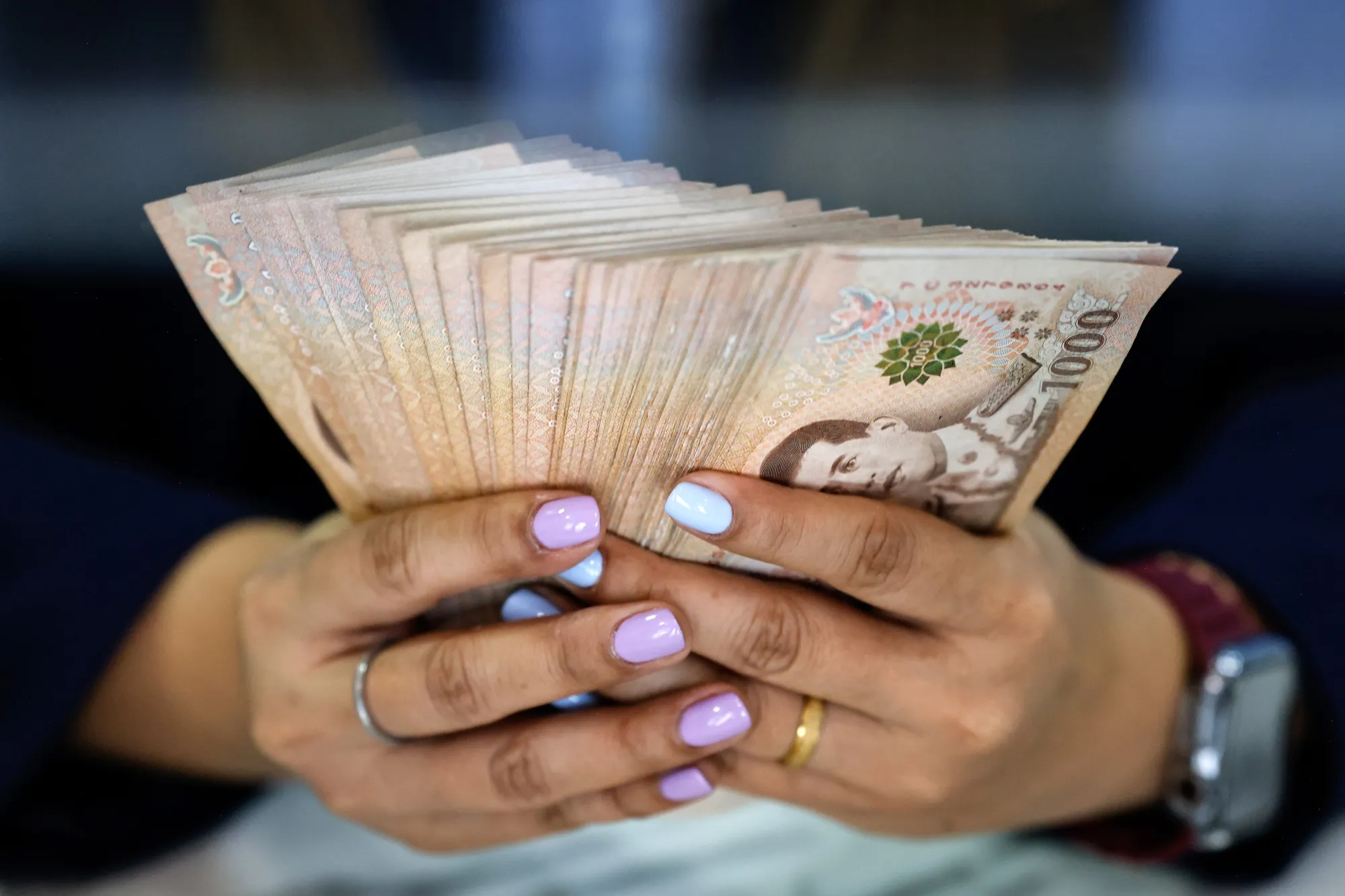 An employee counts 1,000 baht banknotes at a&nbsp;currency exchange store in Bangkok, Thailand.