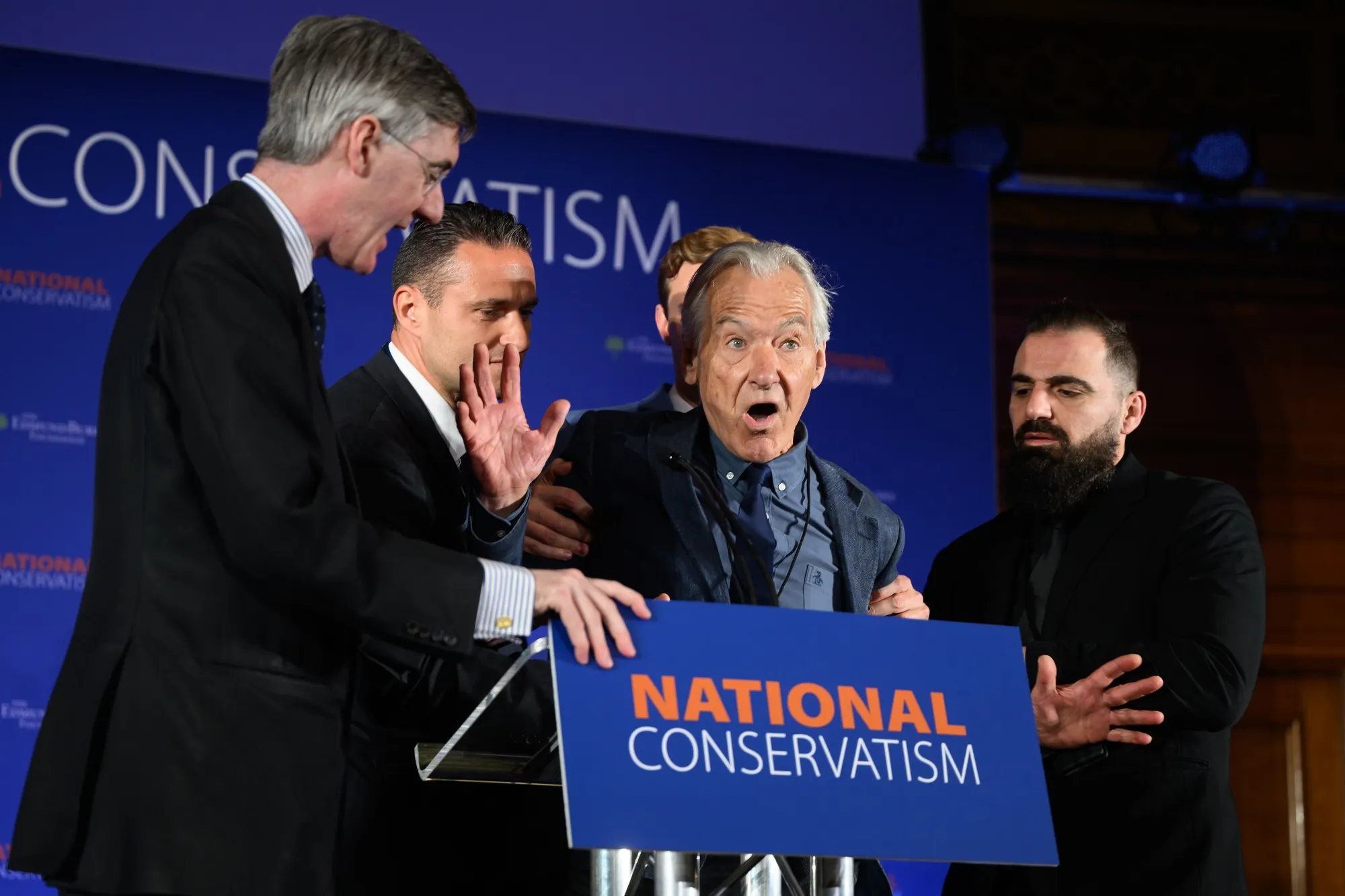 A protestor is escorted from the stage after interrupting a keynote speech by Conservative MP Jacob Rees-Mogg during the National Conservatism conference.