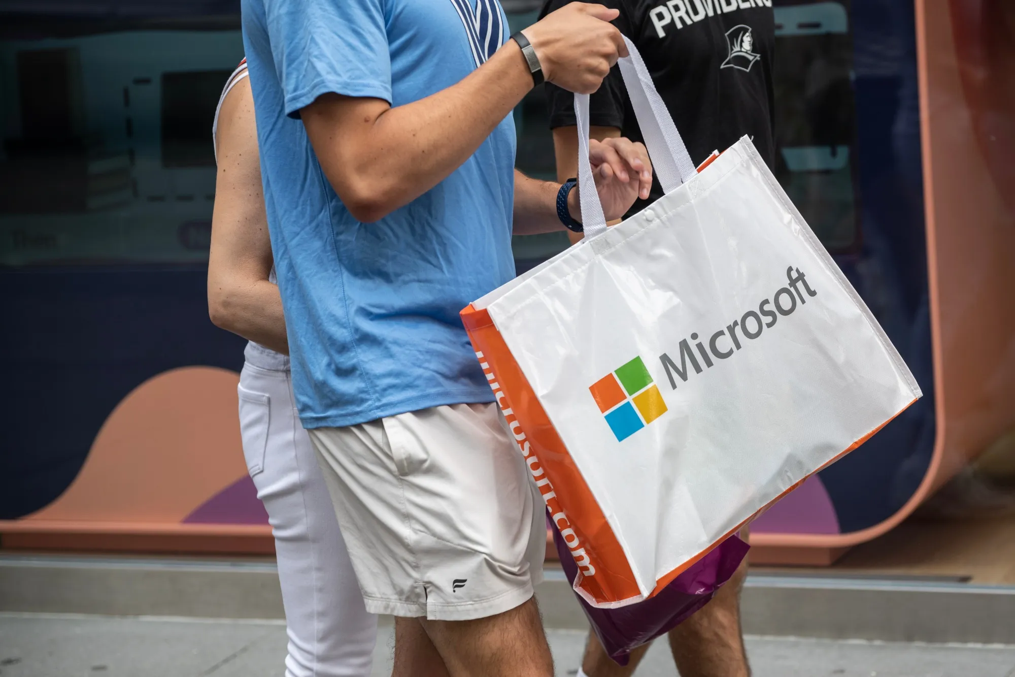 A pedestrian carries a Microsoft shopping bag.