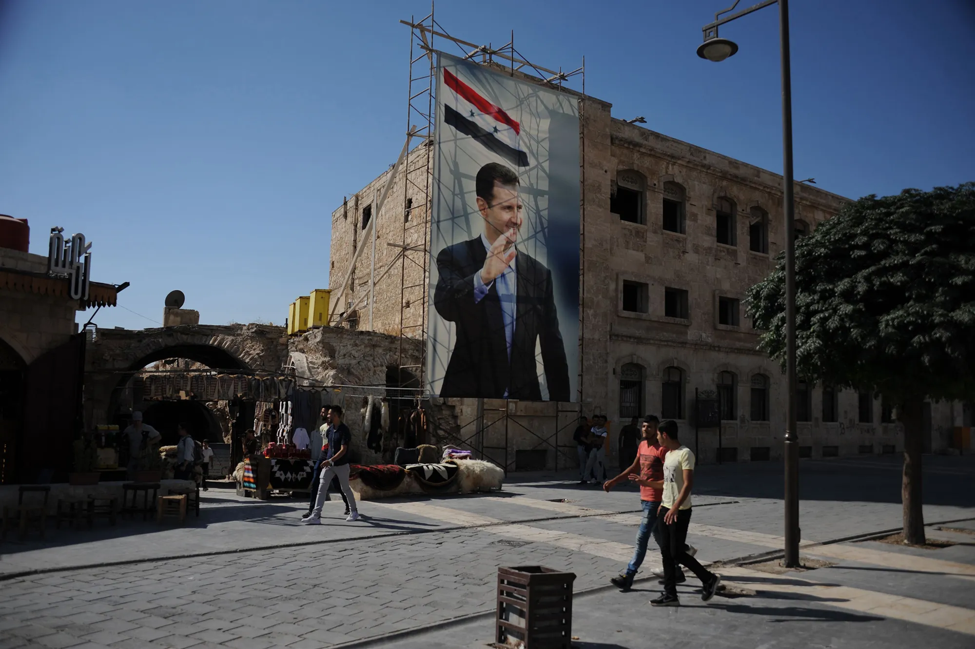 Pedestrians walk past a poster of Bashar al-Assad in Aleppo in 2019.