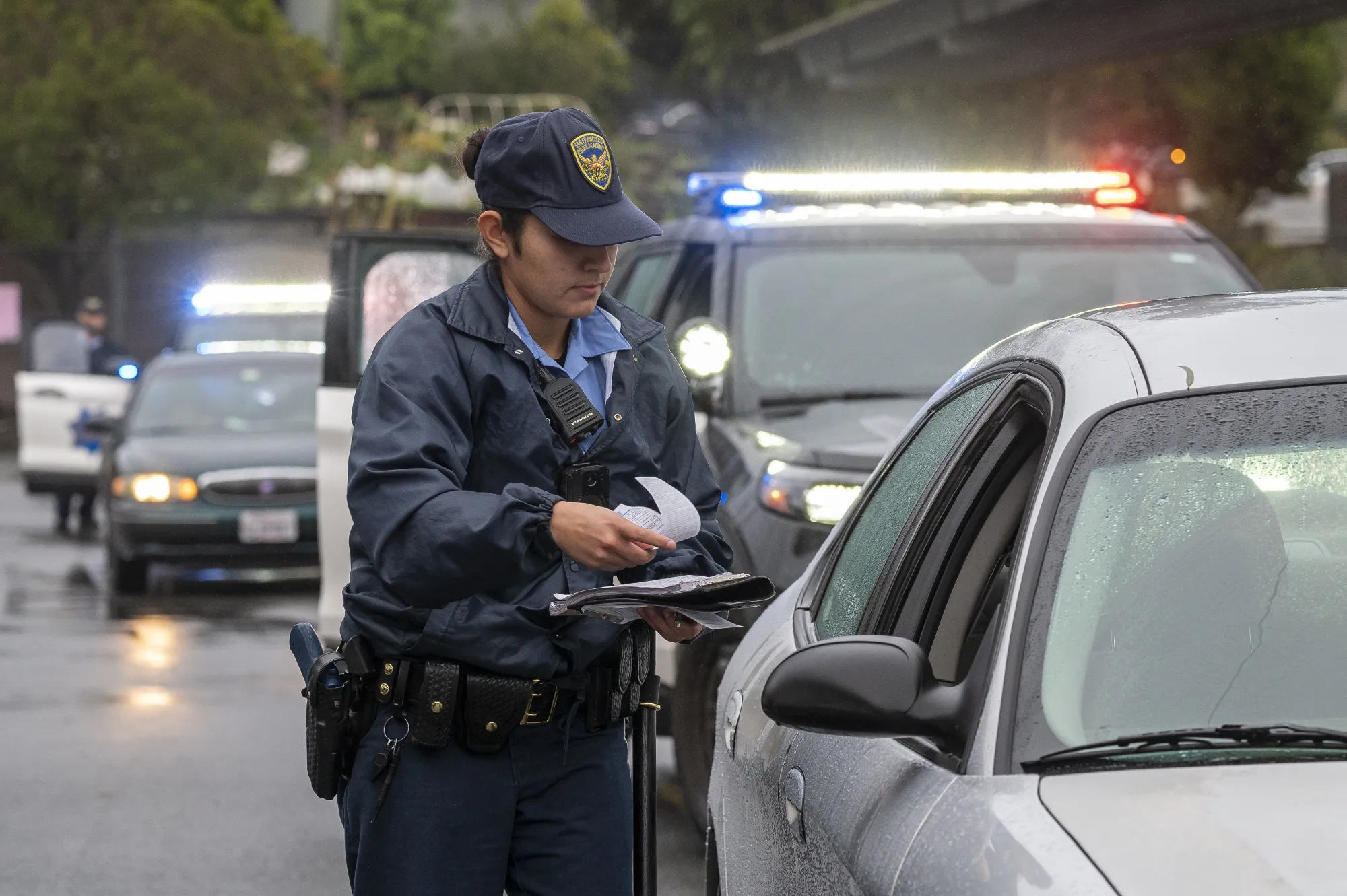 Police officer issuing a citation during a traffic stop in rainy conditions, with patrol cars and emergency lights in the background, highlighting DWI enforcement efforts.