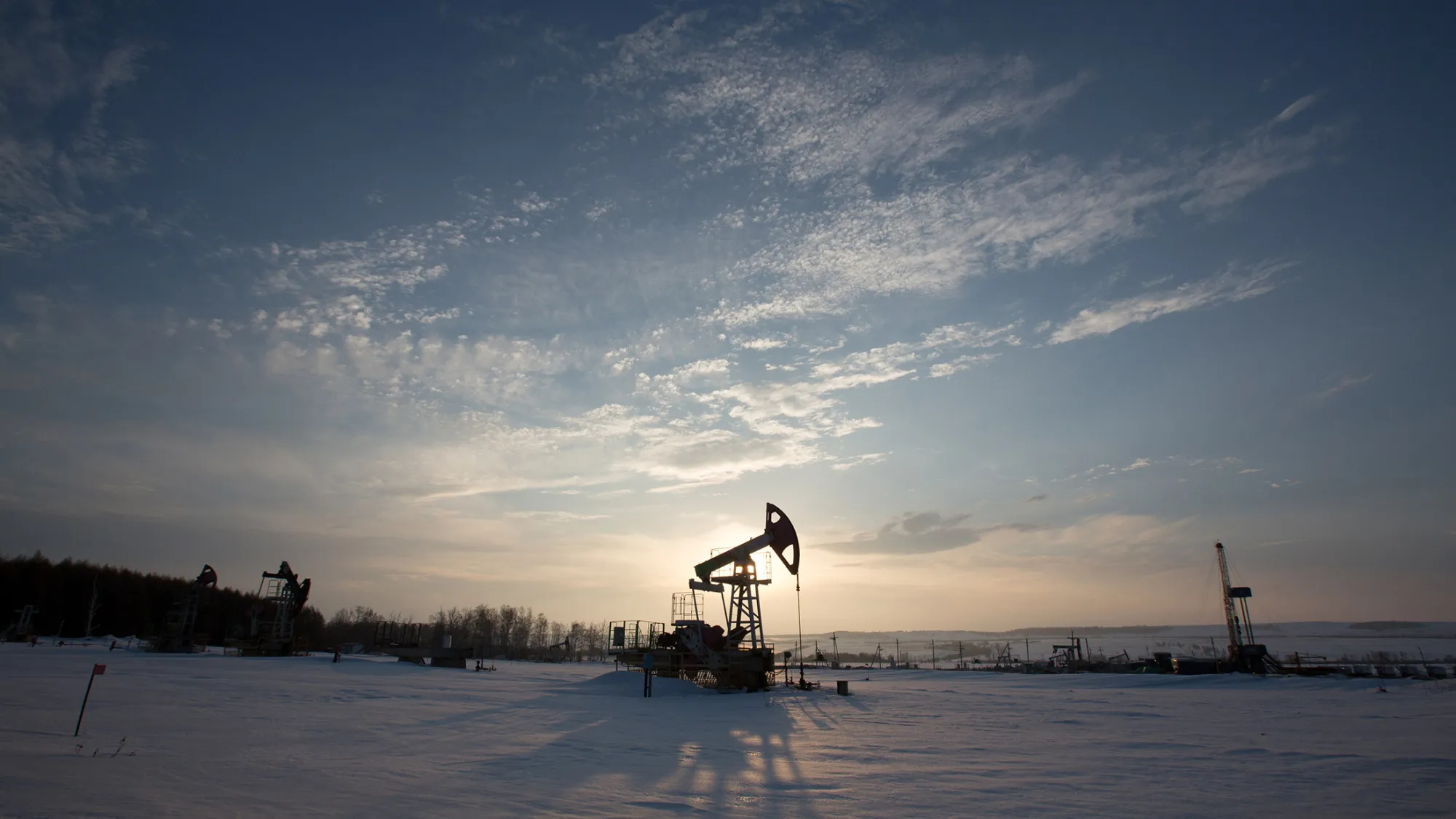 A oil pumping jack, also known as a 'nodding donkey,' operates in a snow covered oilfield near a derrick, right, during drilling operations in an oilfield operated by Bashneft PAO in the village of Otrada, 150kms from Ufa, Russia, on Saturday, March 5, 2016. Bashneft is an upstream and down stream oil &amp; gas provider which explores, produces and refines its own oil and gas which it extracts from brownfield reserves in the Russian Federation.
