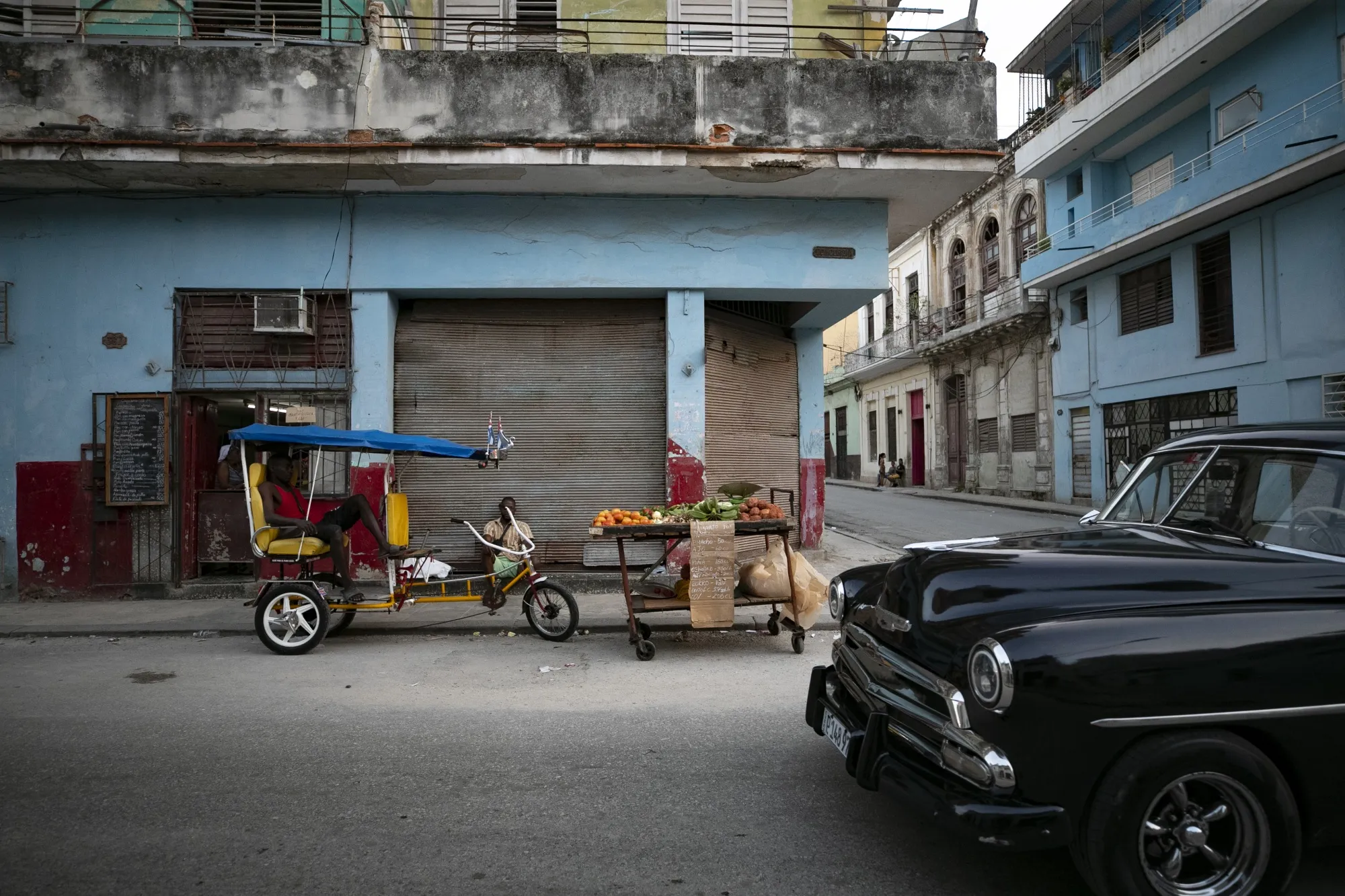 A vehicle drives past a street vendor selling produce in Havana.
