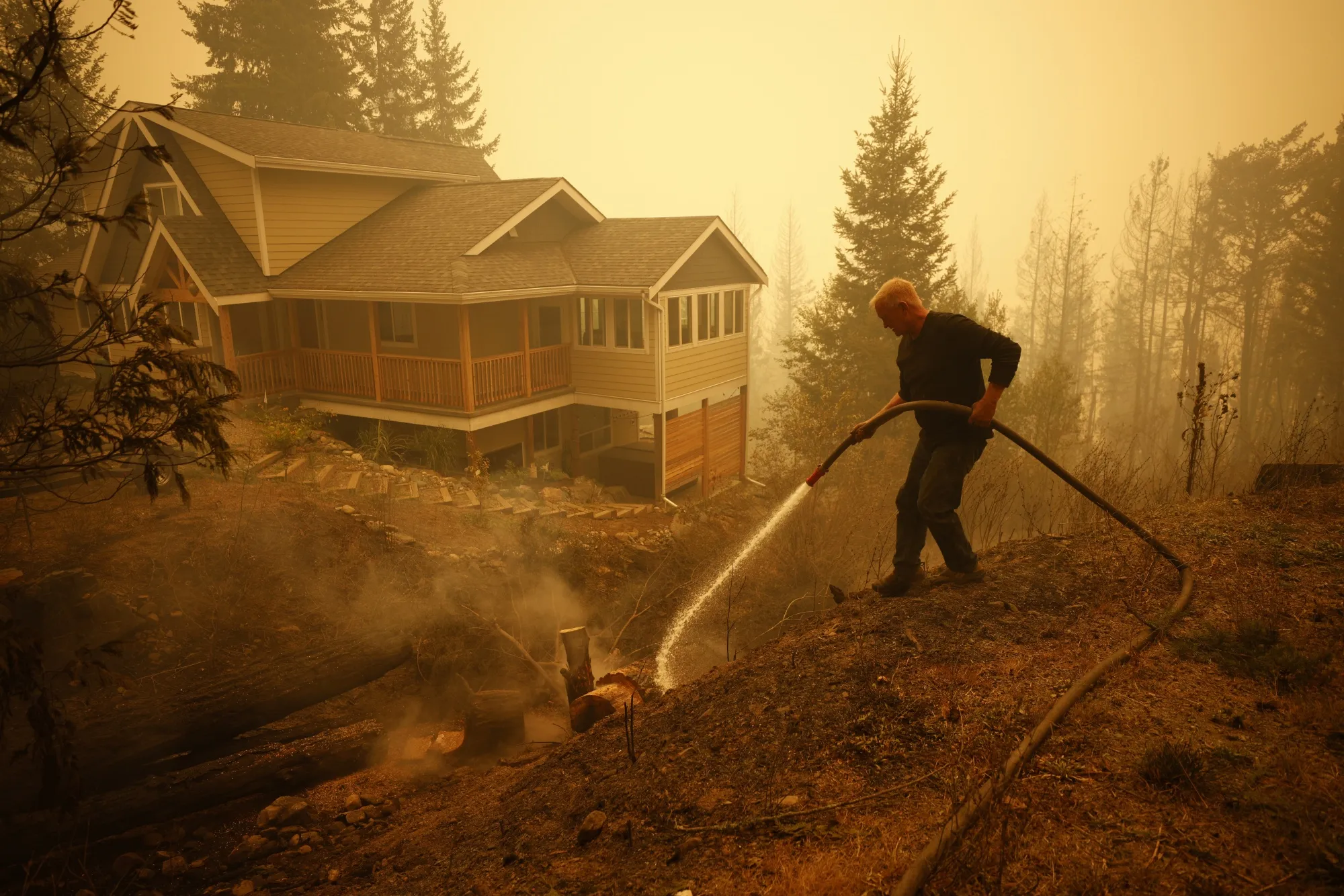 A resident sprays water on hot spots near a house in Celista, British Columbia on Aug. 19. Record-breaking wildfires in Canada have already scorched an area larger than Greece this year.