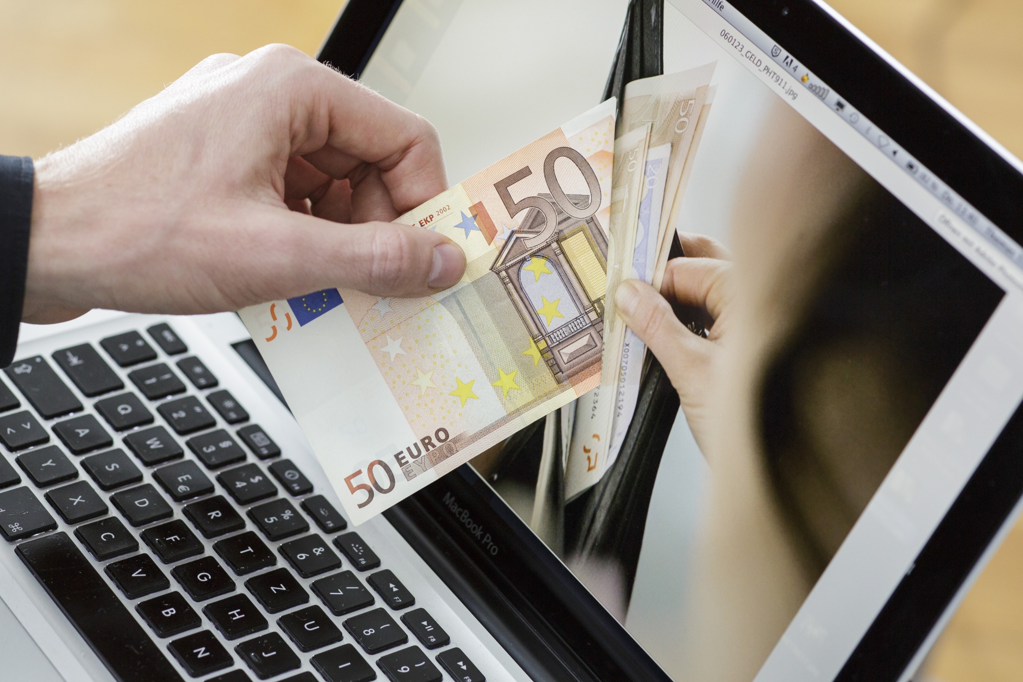 BERLIN, GERMANY - NOVEMBER 21: In this photo illustration a man holds a fifty euro note in front of a computer screen that displays a purse filled with money on November 21, 2013, in Berlin, Germany. The picture symbolizes online money. (Photo illustration gby Thomas Imo/Photothek via Getty Images)