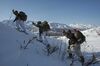Three US soldiers carrying heavy backpacks are snowshoeing uphill, on their way to an avalanche training area. The Alaska Range is in the background.