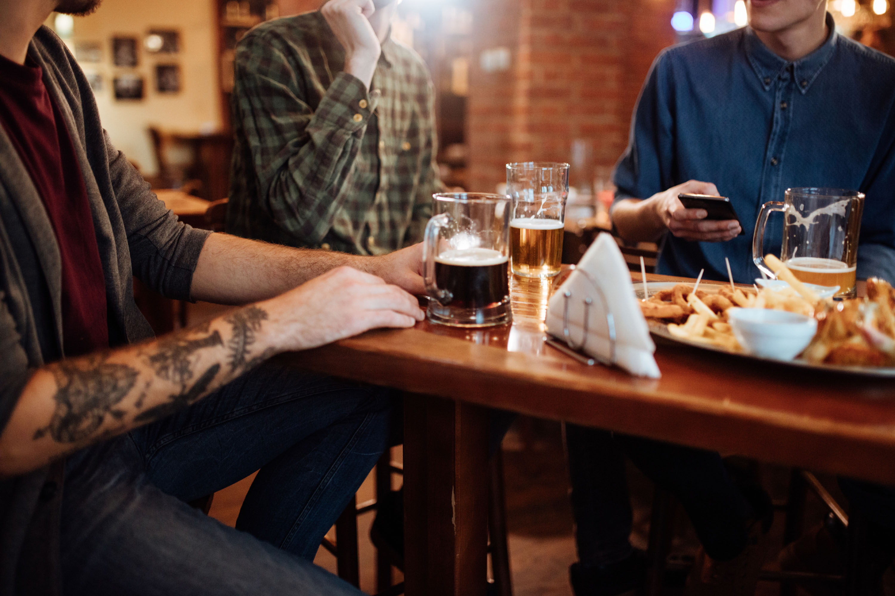 Guys at Pub Drinking Beer and Looking at Smartphone