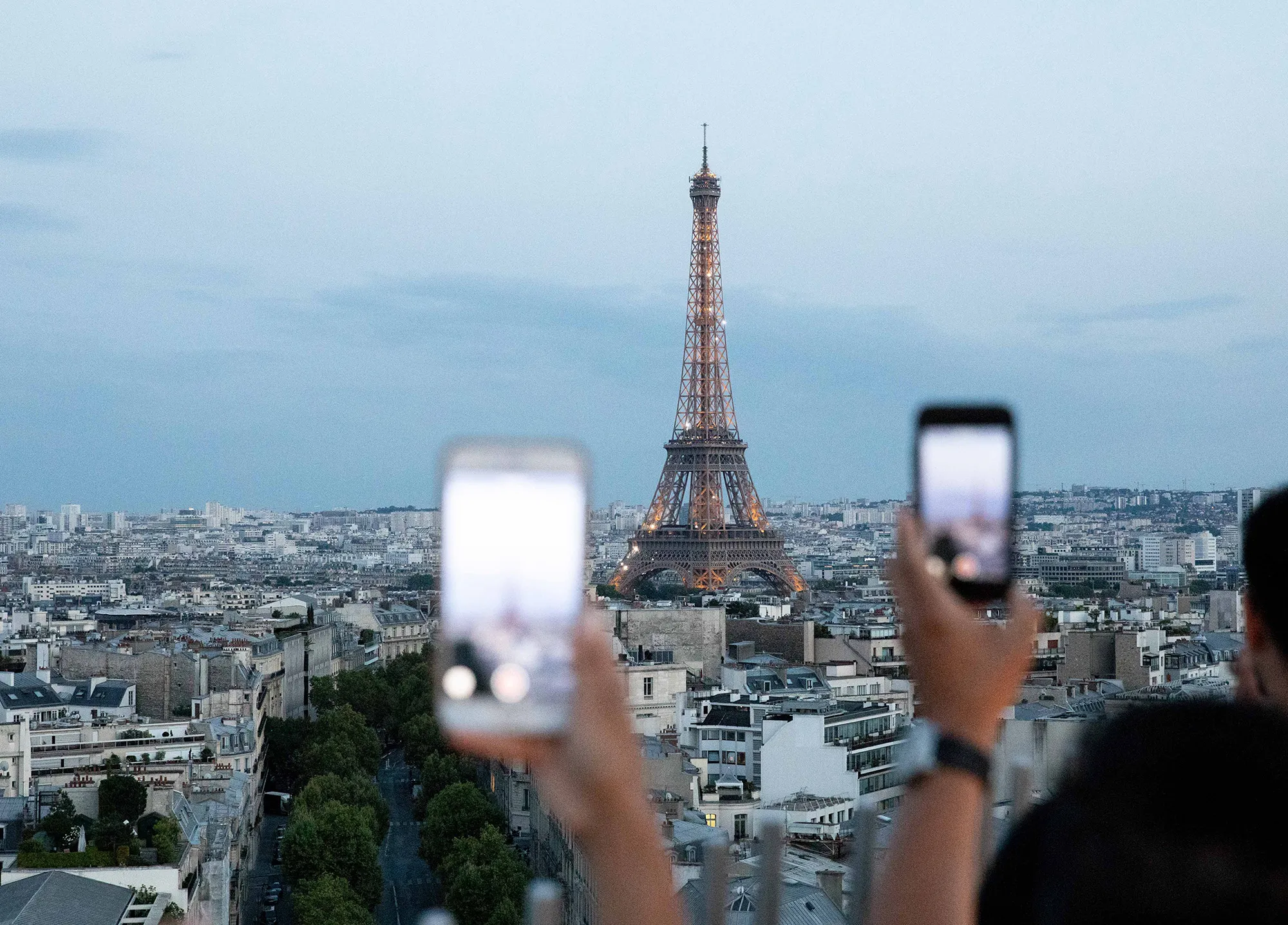 Sightseers use their smartphones to take photos of the Eiffel Tower as it stands above residential and commercial property on the city skyline in Paris.