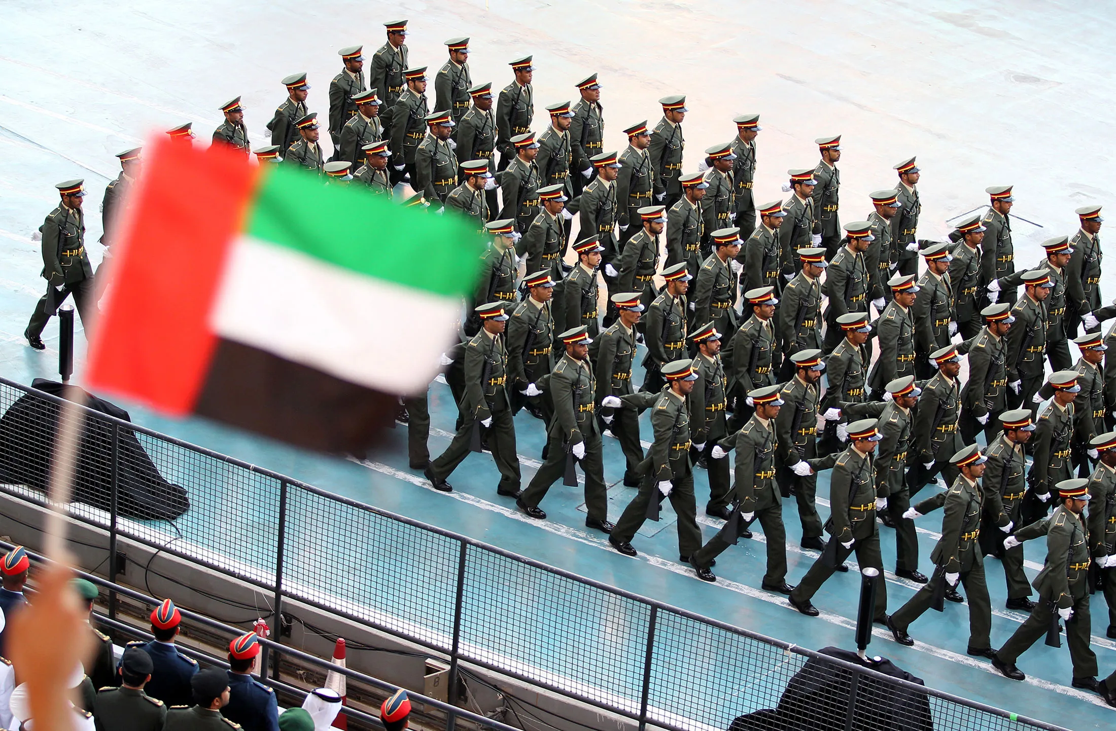 A spectator waves the Emirati flag as troops march.