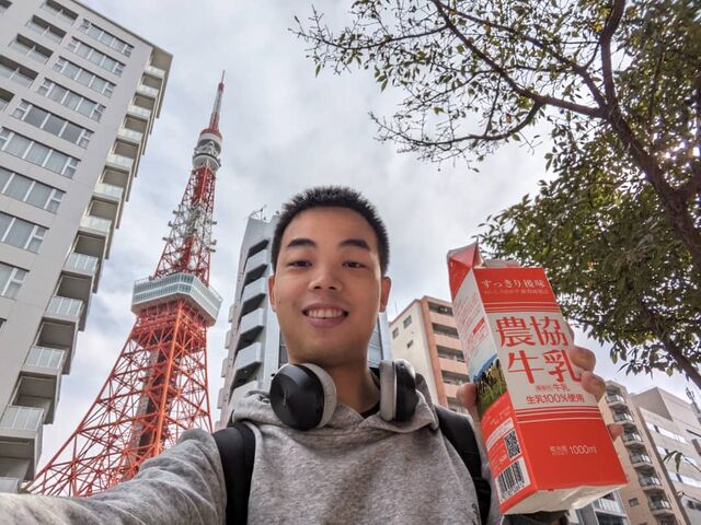 Wang Heng takes a photograph of himself holding a beverage carton in front of the iconic orange-red Tokyo Tower.
