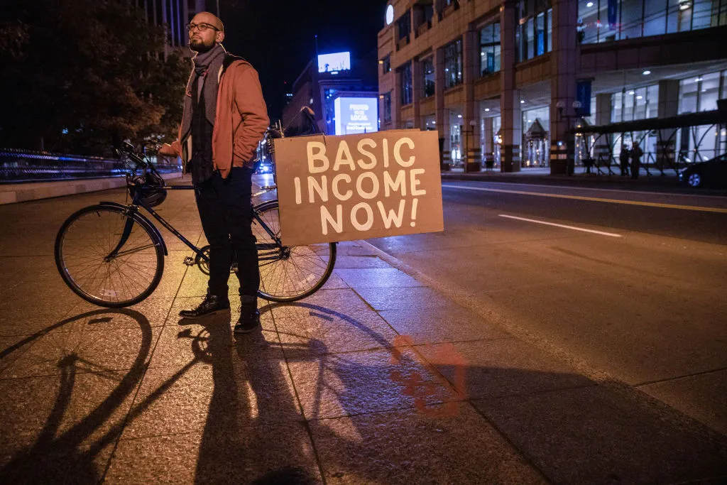 A man holds a sign advocating for basic income during a 2020 rally in front of the Ohio Statehouse.&nbsp;