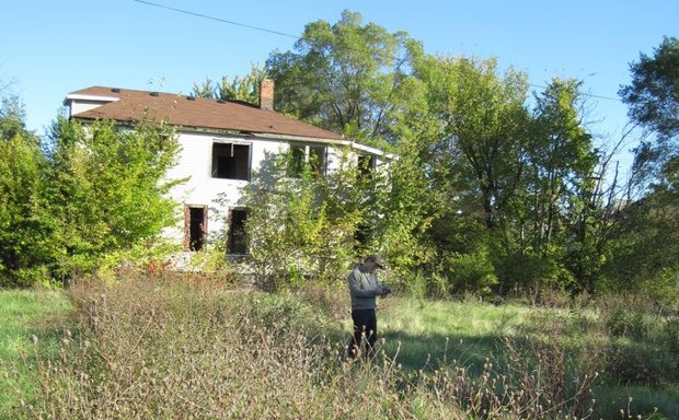 A researcher collects pollen data next to an abandoned home in Detroit.
