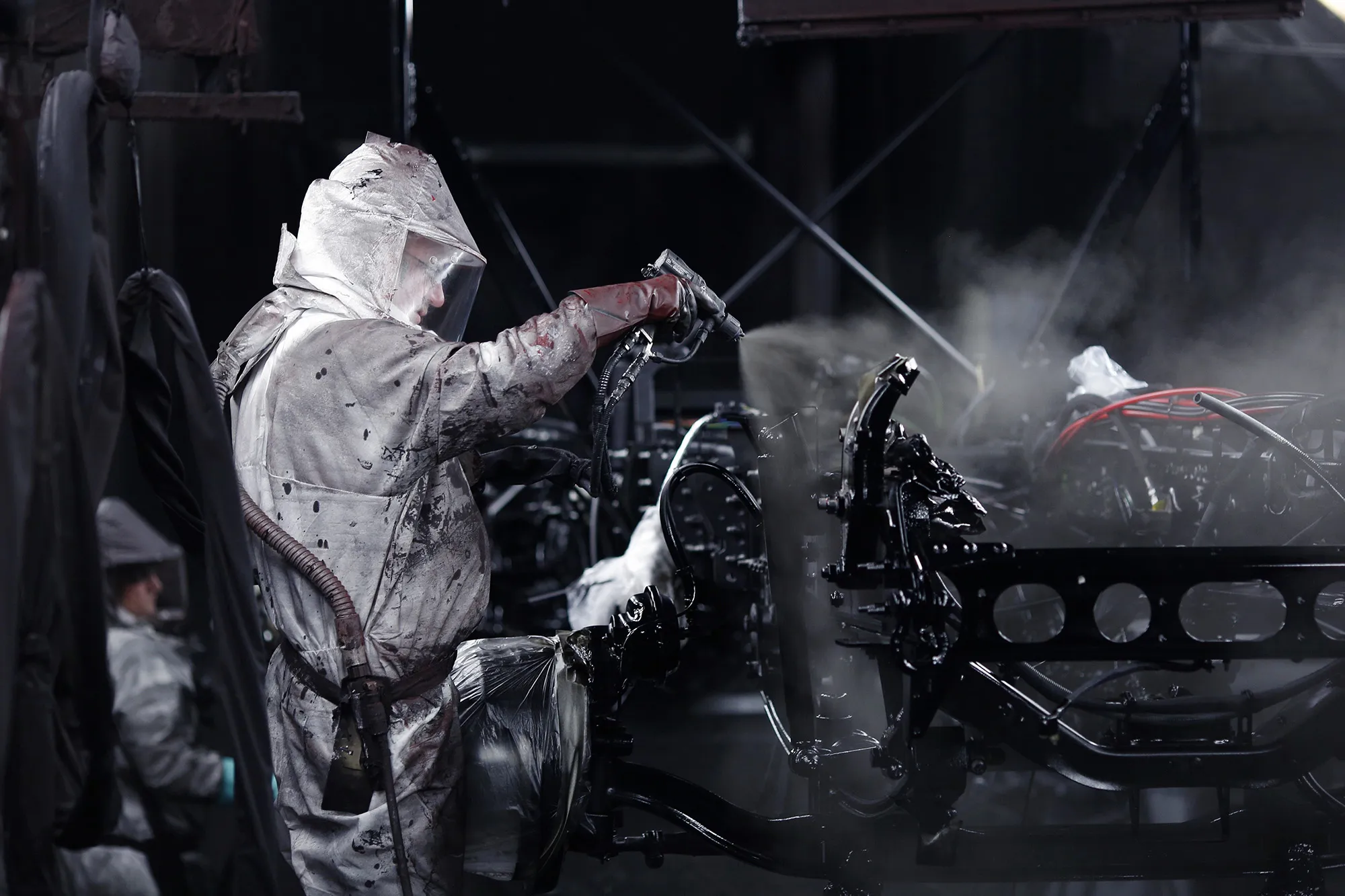 Workers wearing protective suits paint a semi truck chassis inside a paint booth at a vehicle assembly facility in Macungie, Pennsylvania.