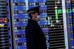 A passerby with a face mask walks past a stock board in Tokyo's Nihonbashi district. 