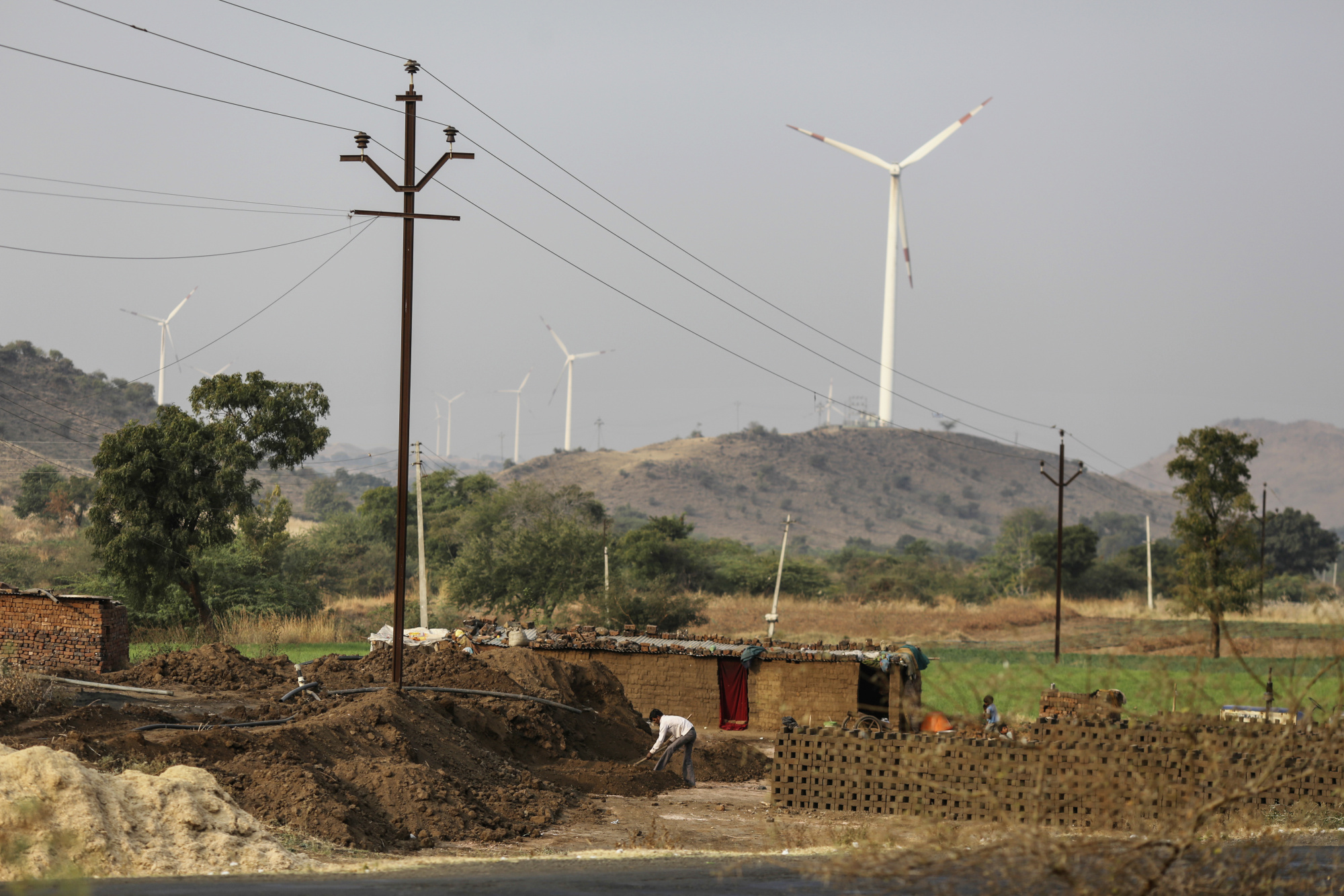 Laborers work below an electricity pole operated by Maharashtra State Electricity Distribution Co. (MSEDCL) as Suzlon Energy Ltd. wind turbines stand in the background in Nadurbar district, Maharashtra, India, on Tuesday, Jan. 17, 2017. Indian Prime Minister Narendra Modi pledged to bring reliable power to all citizens during the campaign that propelled him into office in 2014, the same year the World Bank pegged India as home to the world's largest un-electrified population. While his government has made progress meeting its 2019 deadline, many families are still missing out, holding back some of India's poorest, most-vulnerable citizens and preventing the country from achieving its development ambitions.