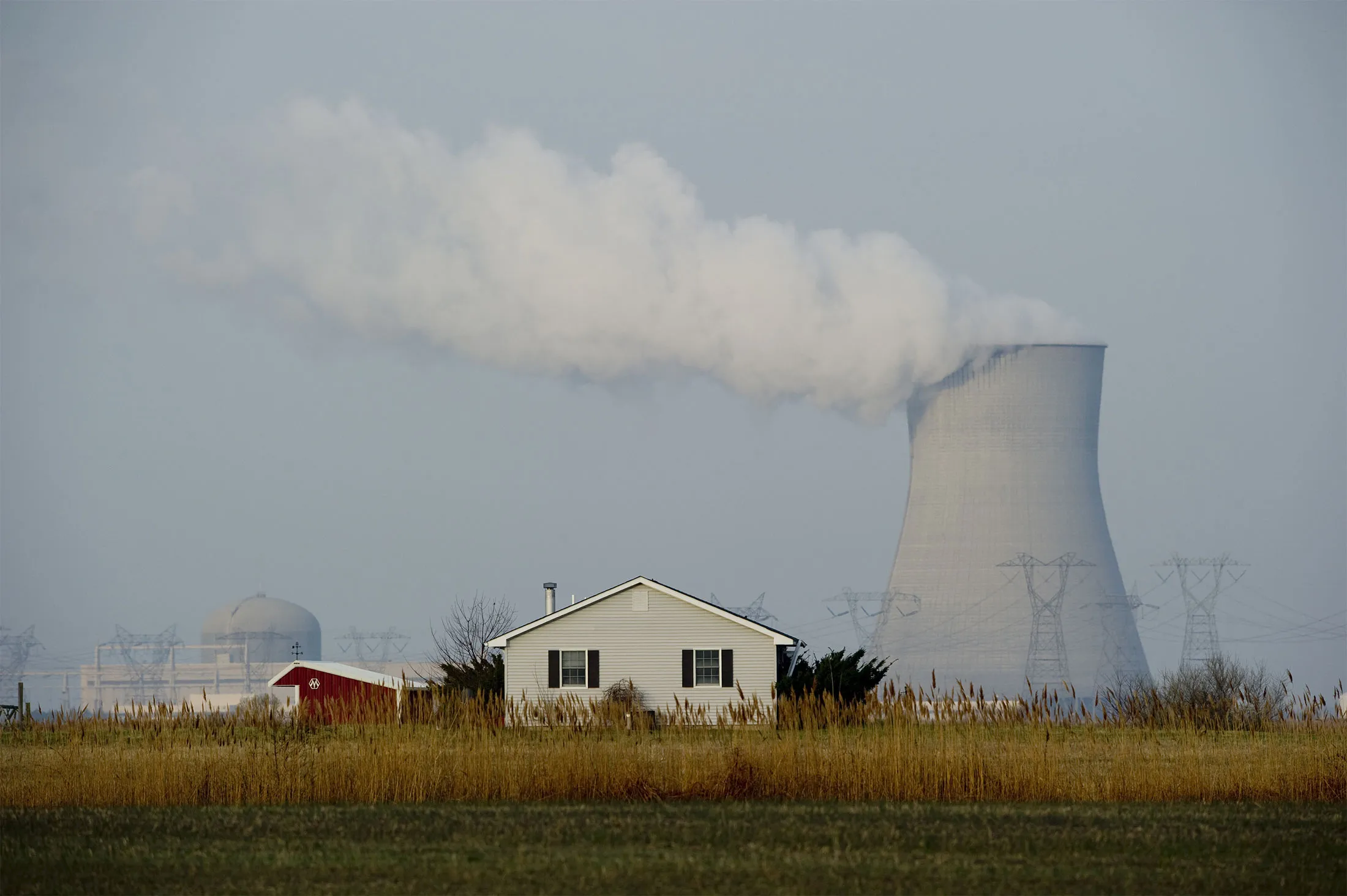 The Hope Creek Nuclear Generating Station (L, dome) and cooling tower (R) seen in the distance behind a farmhouse&nbsp;