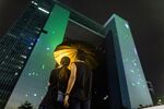 Demonstrators stand under an umbrella on Harcourt Road as laser lights are projected on the Central Government Offices during a protest in the Admiralty district of Hong Kong, China, on Sunday, Aug. 18, 2019.