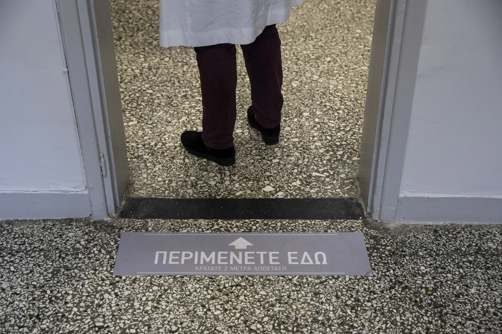 A health-care worker waits by a&nbsp;sign reading 'Wait Here. Please Keep 2 Meters Distance,' at the entrance of the vaccination hall of Evangelismos hospital, in Athens.