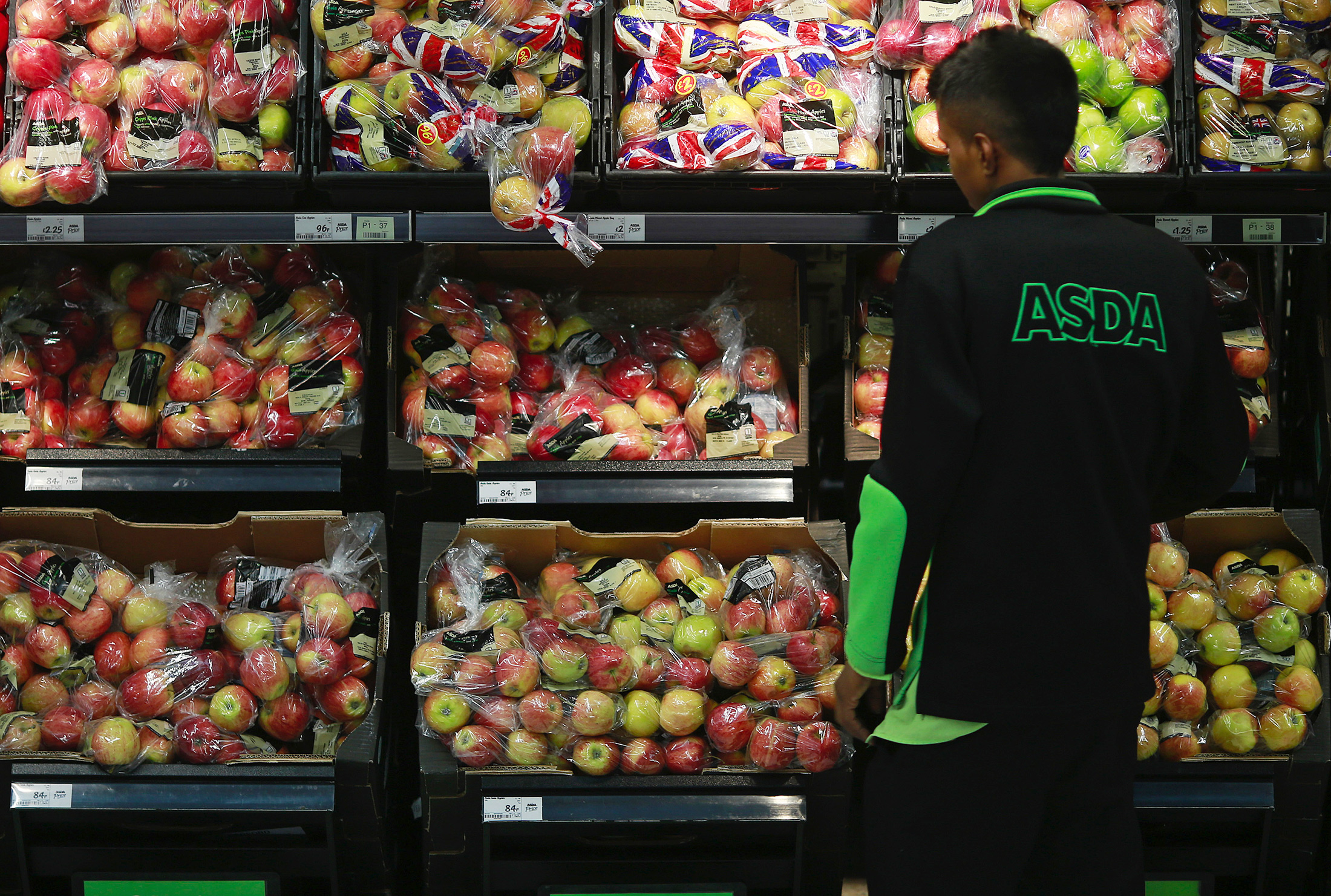 An employee checks the stock levels of an apple display in the fruit and vegetable section of an Asda supermarket in London.