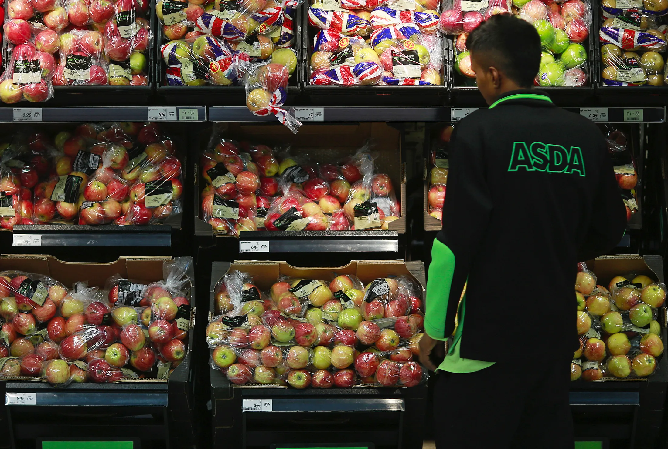 An employee checks the stock levels of an apple display in the fruit and vegetable section of an Asda supermarket in London.