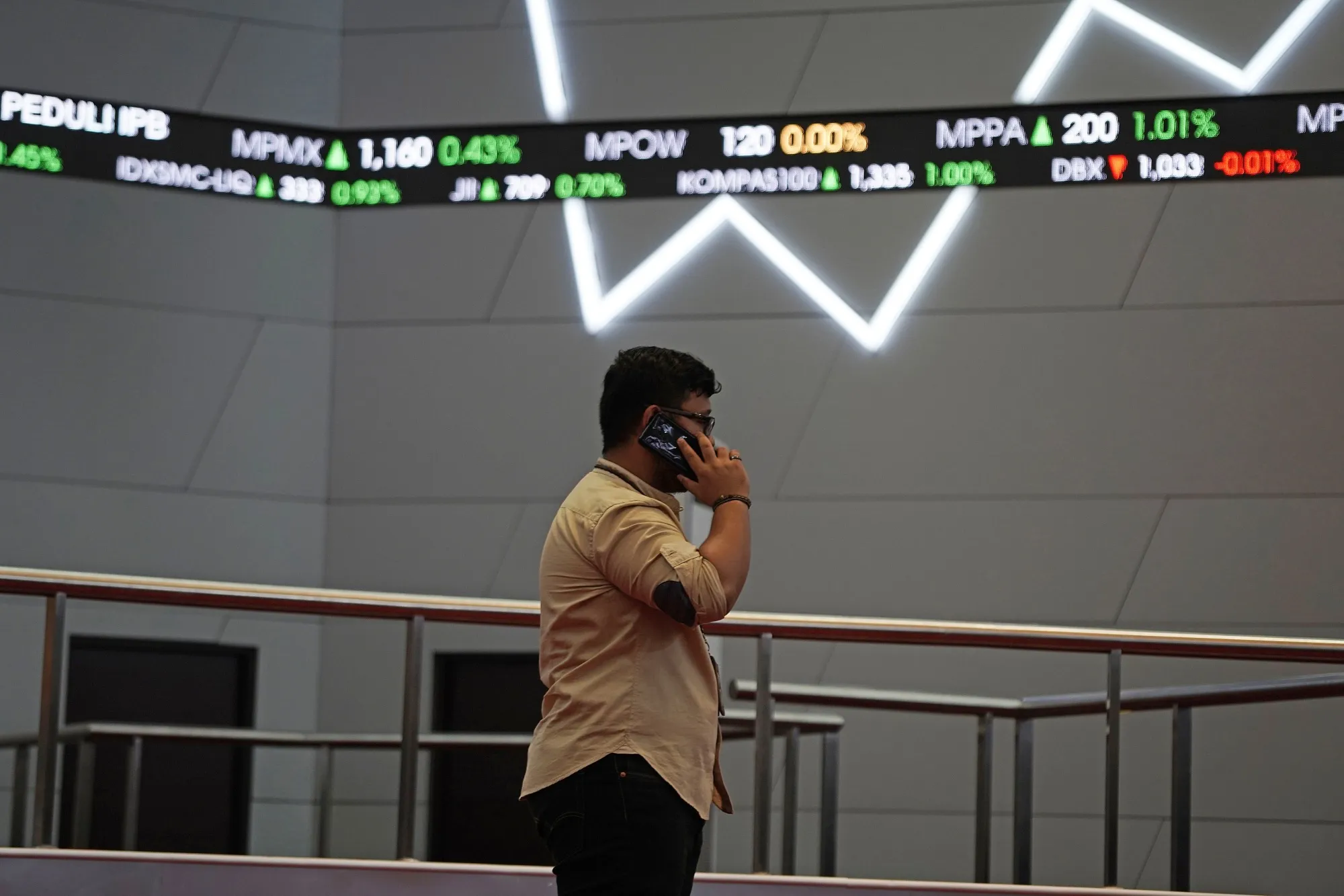 A man uses a mobile phone as tickers display stock prices inside the Indonesia Stock Exchange (IDX) in Jakarta, Indonesia, on Thursday, April 18, 2019.