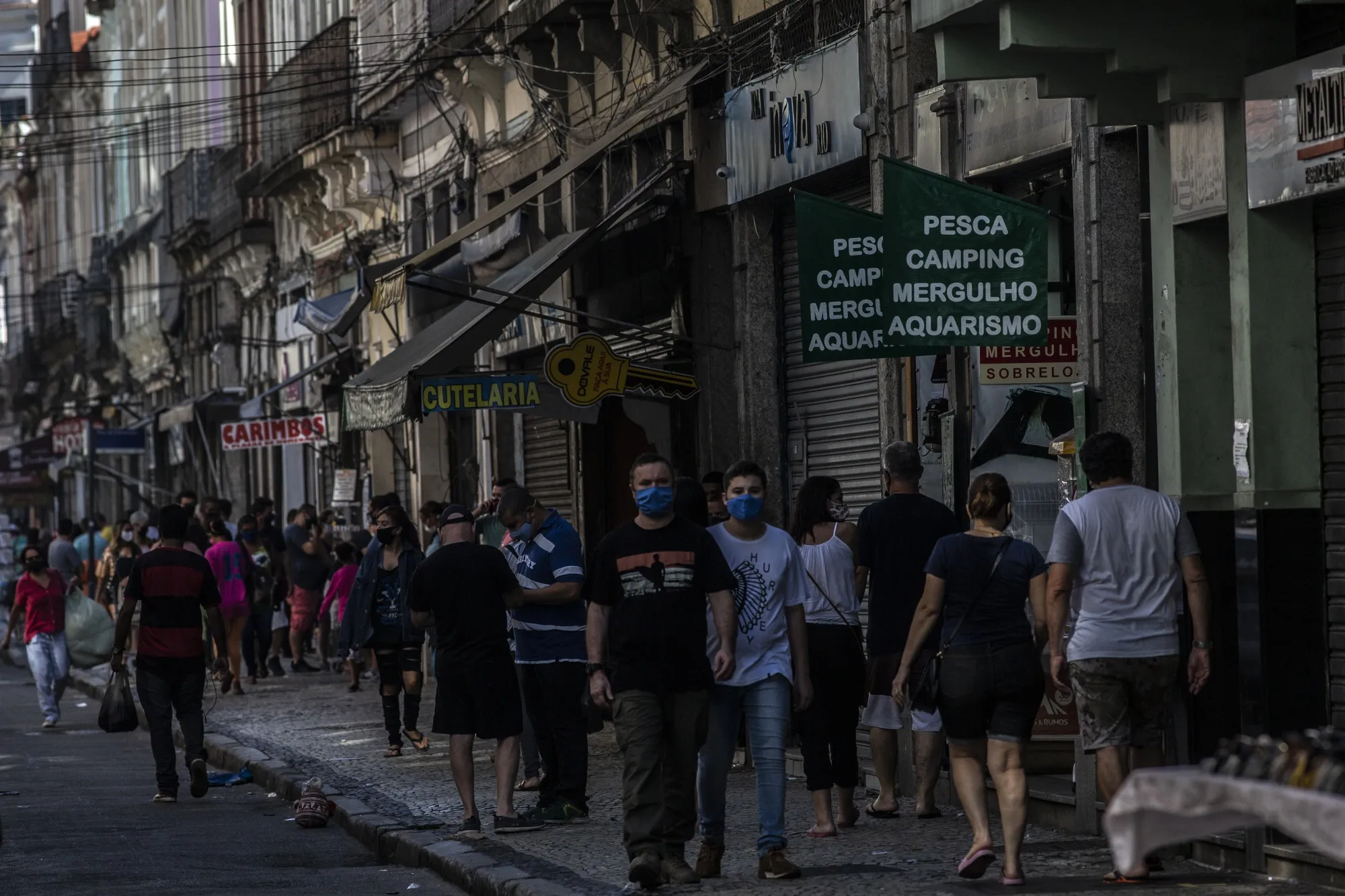 People wearing protective masks walk past partially opened businesses in downtown Rio de Janeiro, Brazil.