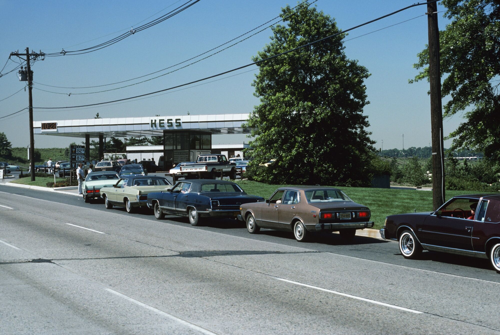 1970s CARS LINED UP AT GAS...